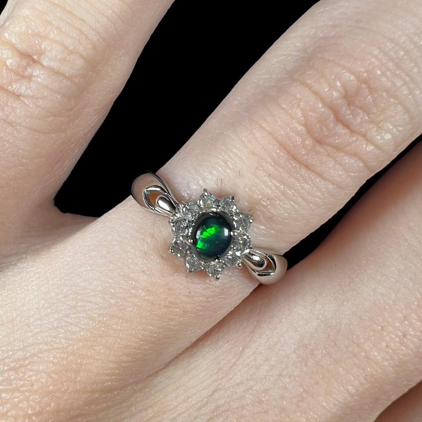 Macro shot of black opal ring on hand showing bright green flash in center stone.