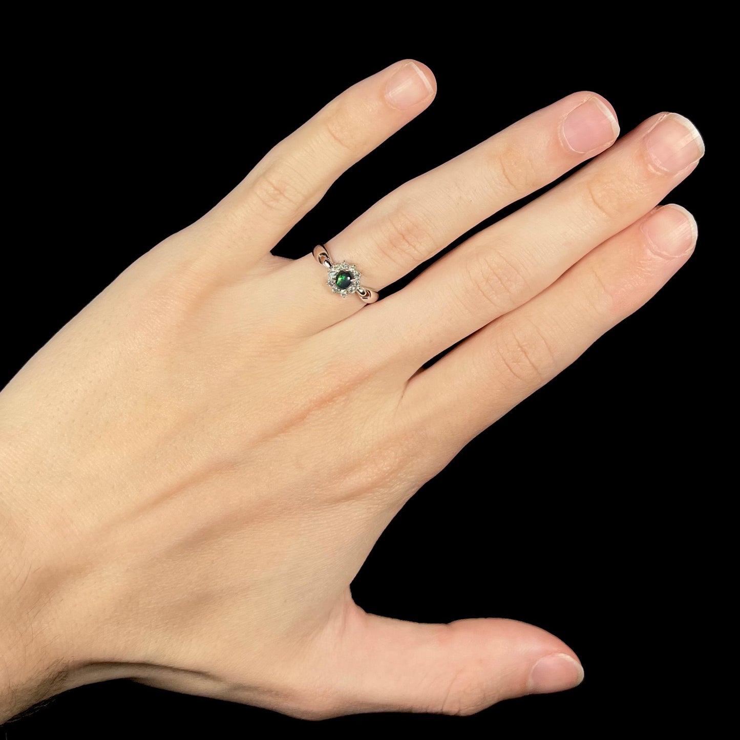 Black opal engagement ring worn on hand with visible green color play in opal.