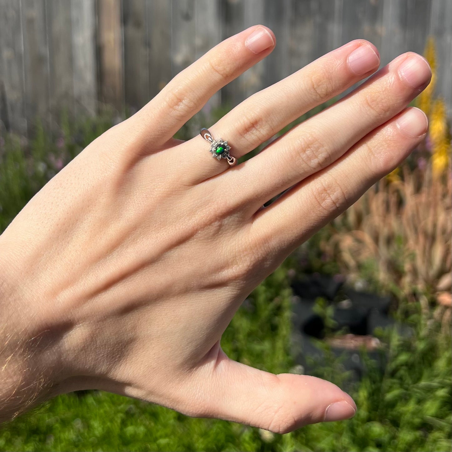 Black opal ring in natural sunlight showing bright green flash with outdoor background.