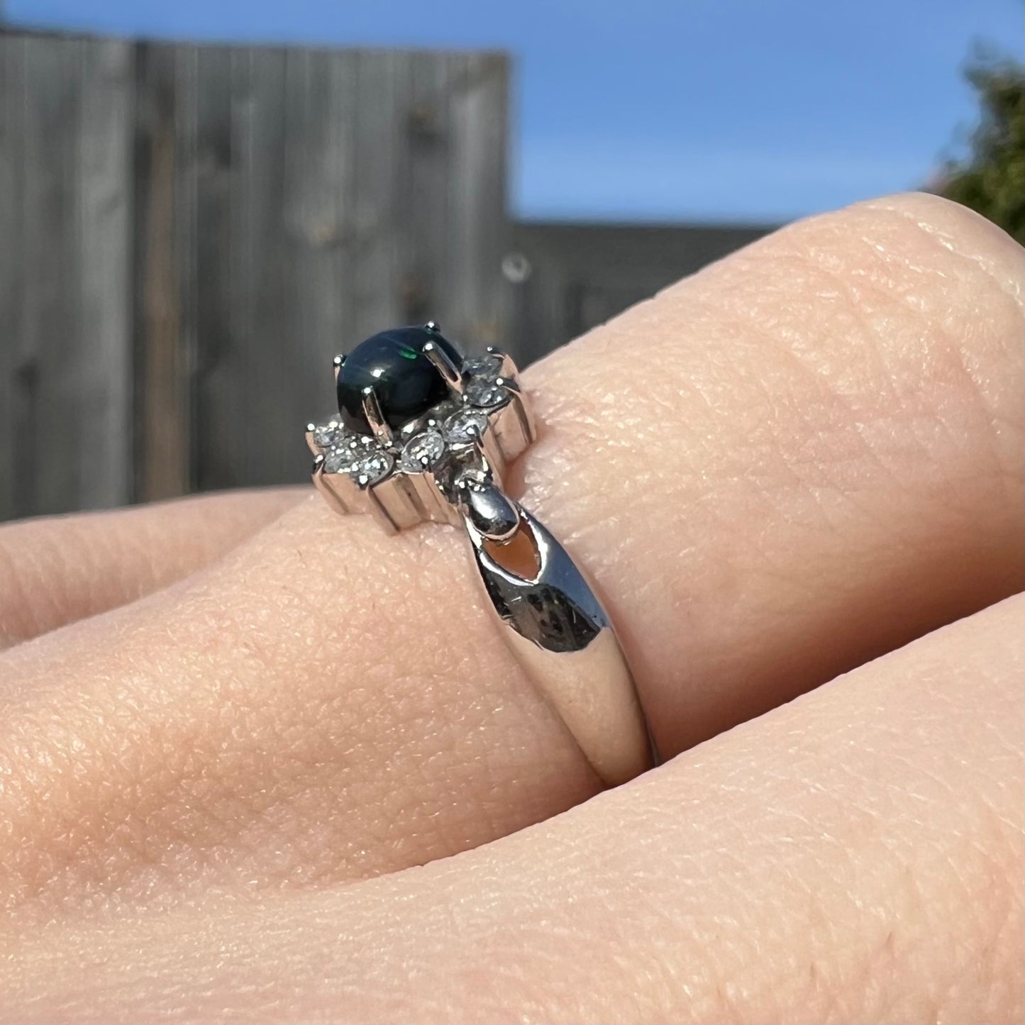 Side angle outdoor view of black opal ring with mostly black opal and tiny green flash.