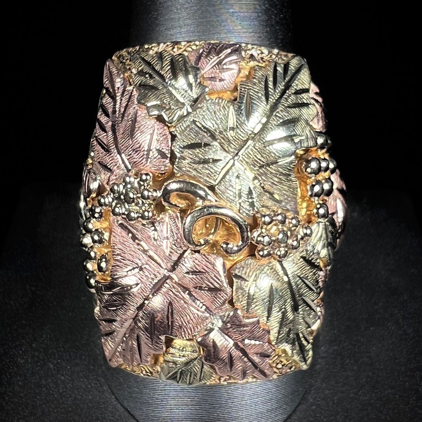A men's solid gold ring. The ring is Black Hills gold featuring a grapevine and leaf motif with rose and green gold designs.