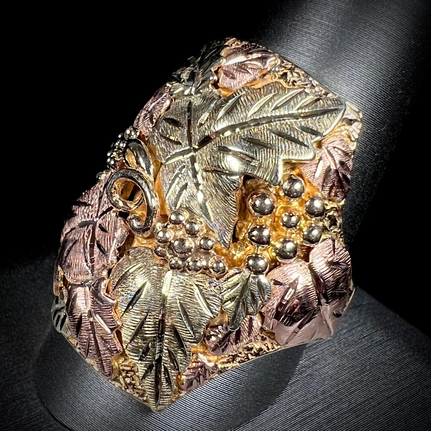 A men's solid gold ring. The ring is Black Hills gold featuring a grapevine and leaf motif with rose and green gold designs.