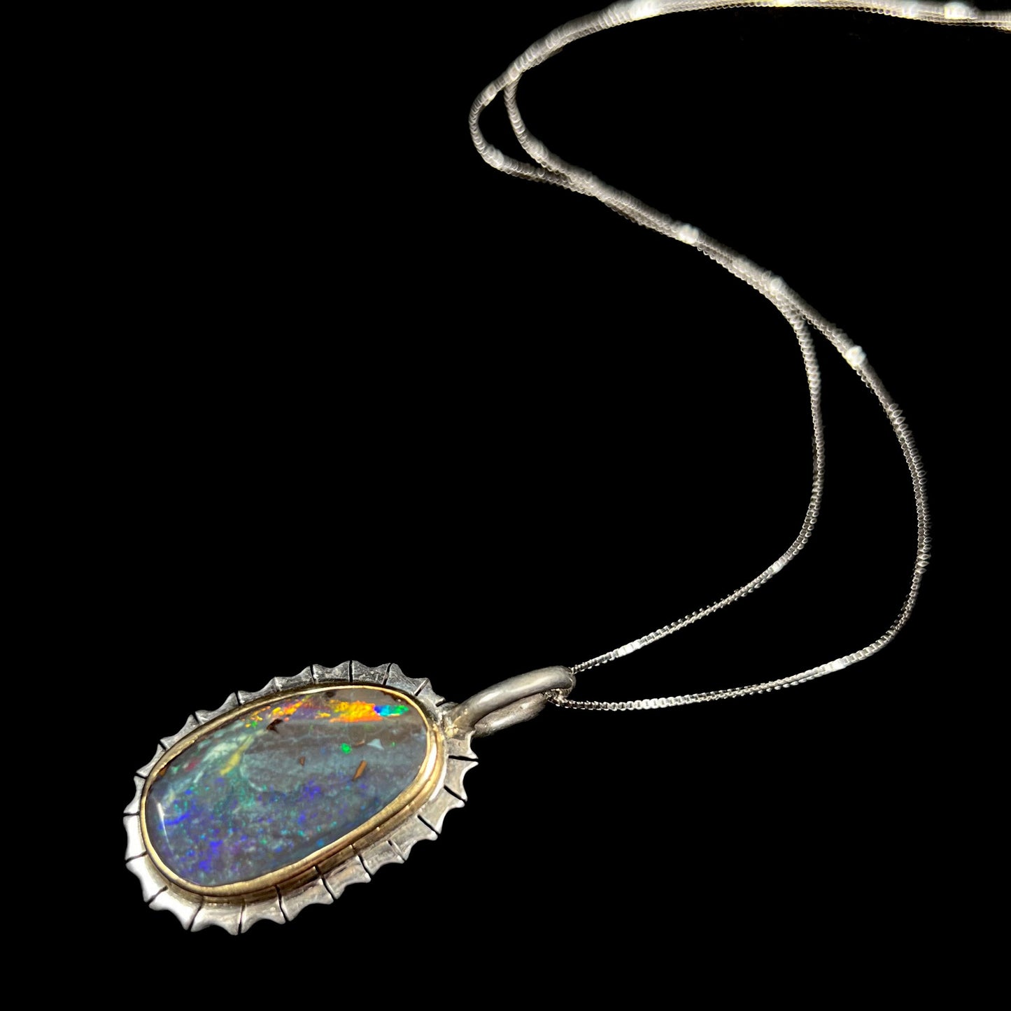 A Southwest style two-tone sterling silver pendant set with a black boulder opal with a yellow gold bezel.