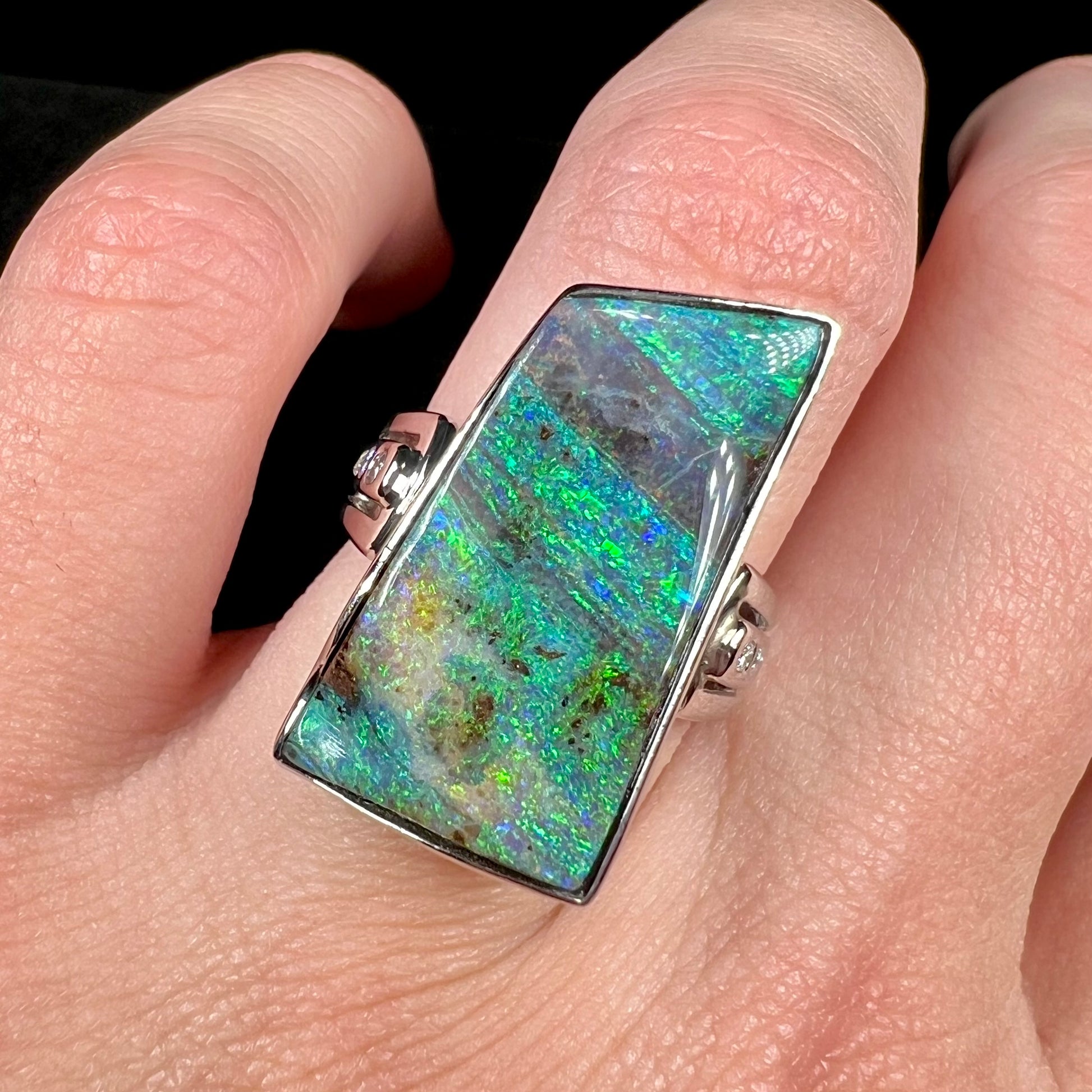 Close-up view of a blue-green, freeform shaped Australian boulder opal ring on a hand.