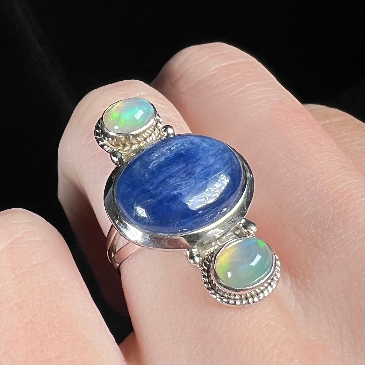 A blue kyanite cabochon ring with two Ethiopian opal accents, worn on a finger and shown at an angle.