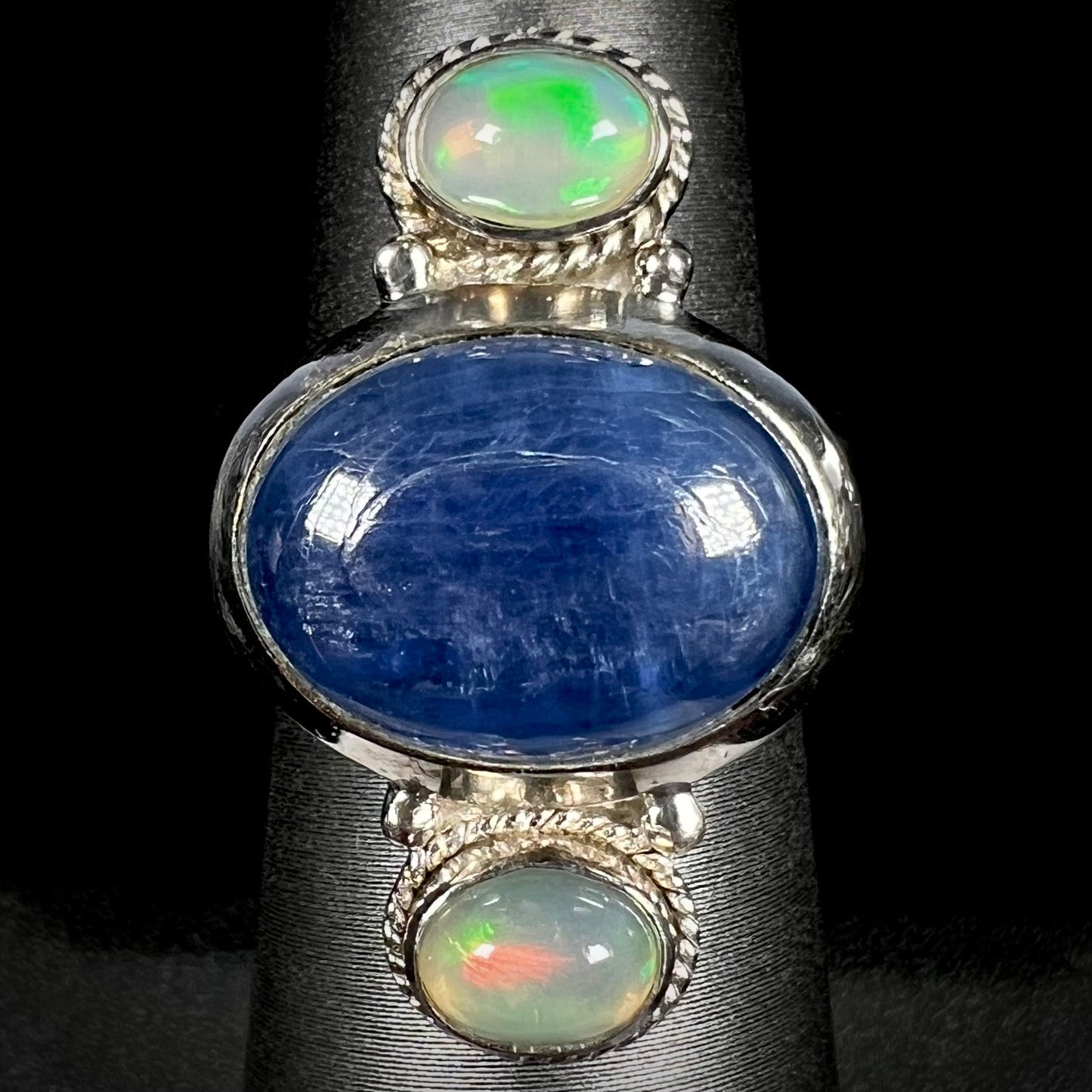 Front view of a blue kyanite cabochon and Ethiopian opal-accented silver ring against a black background.