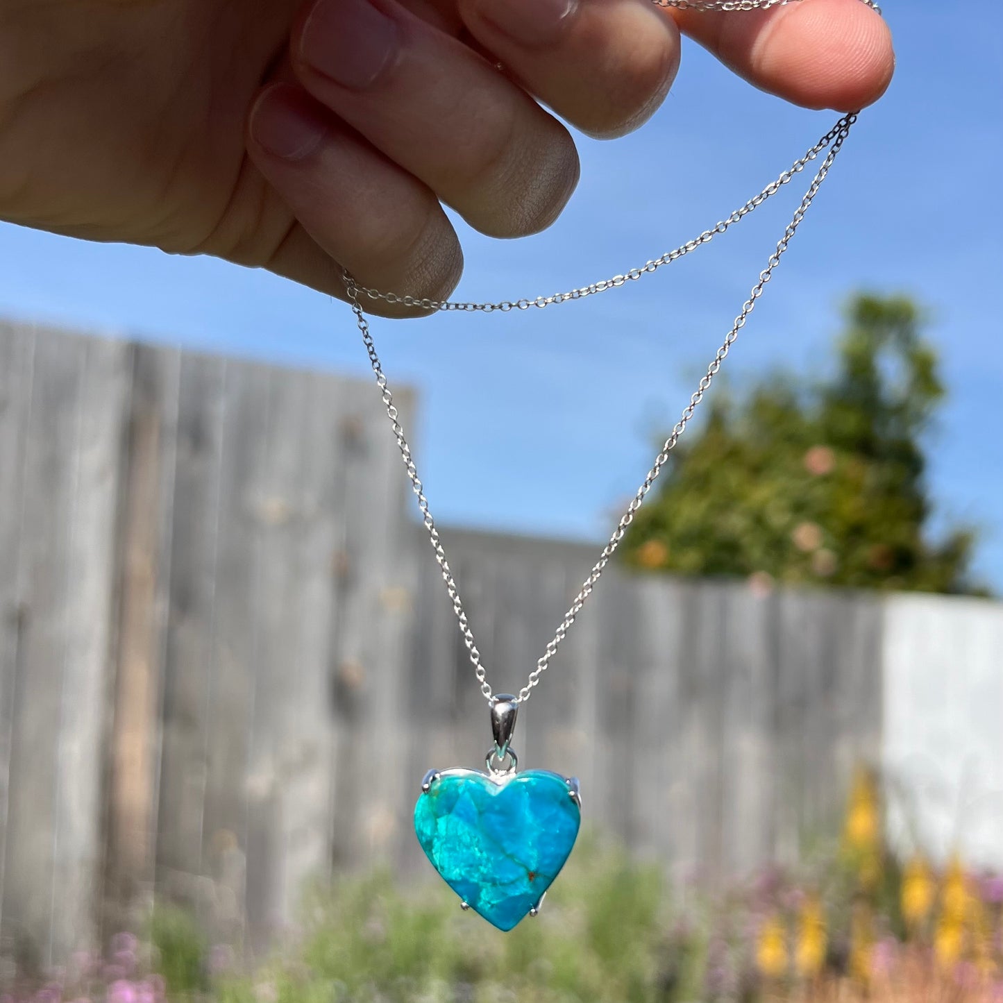 Chilean blue opal heart necklace held in sunlight, showing vivid body tone.