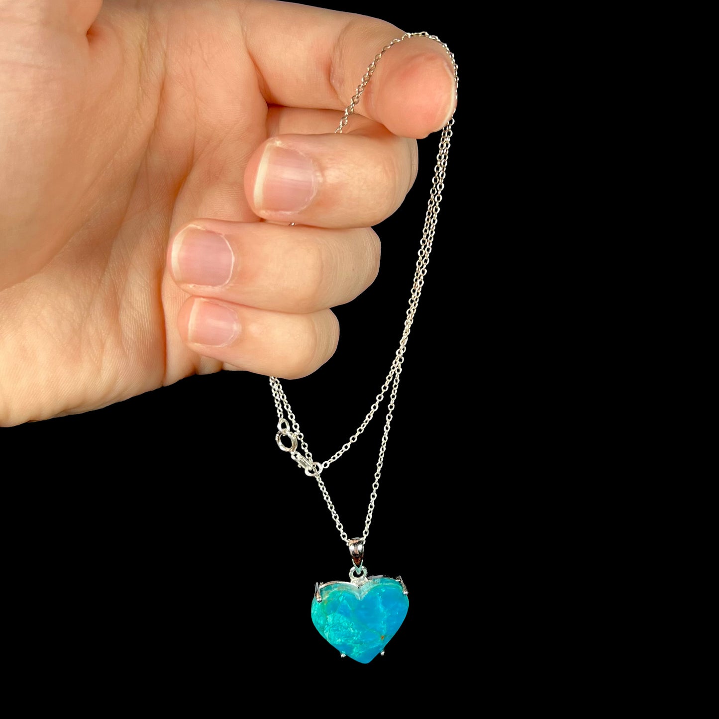 Natural blue opal heart necklace being held by the chain against a black background.