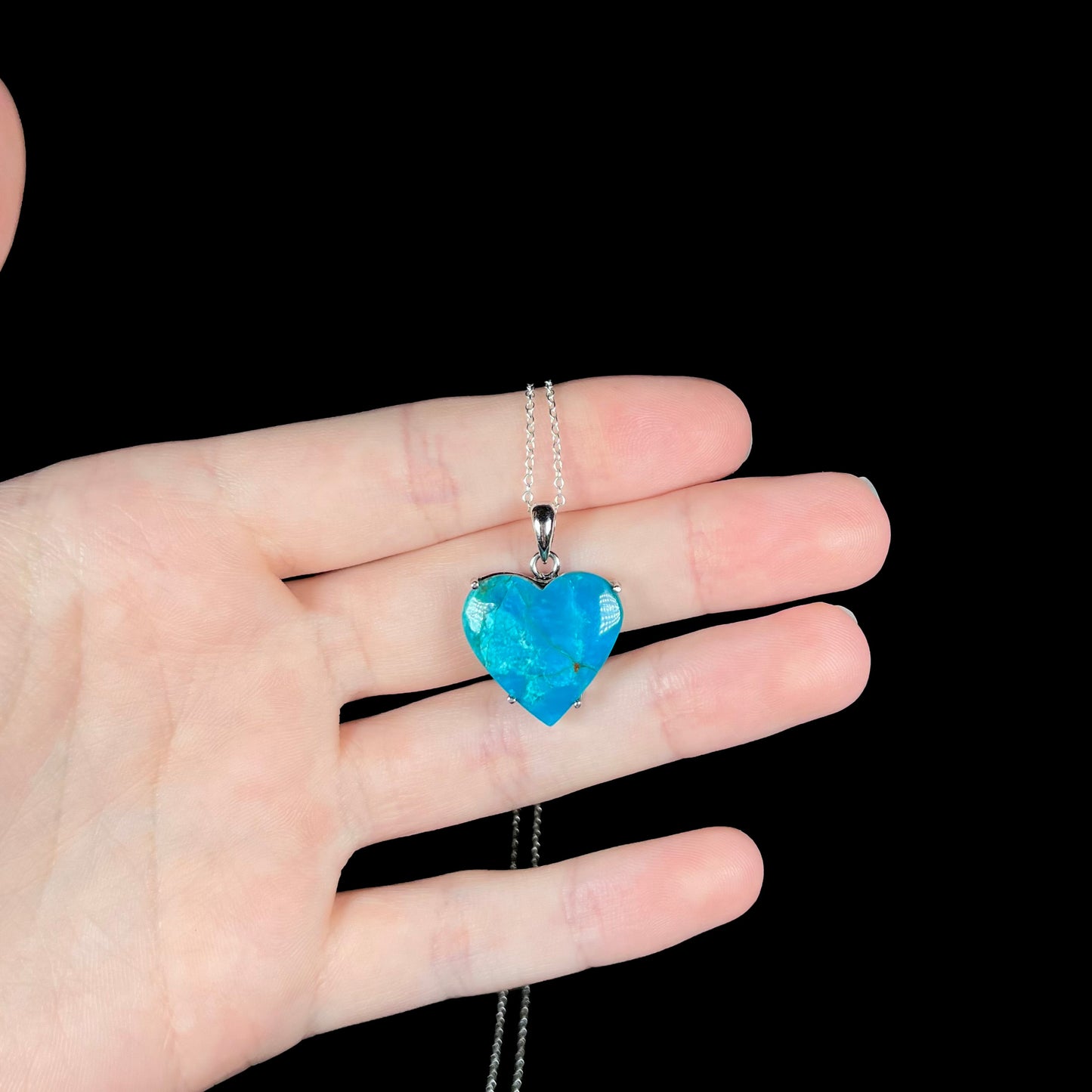 Heart-shaped Chilean opal necklace resting across fingers with vibrant blue coloring.