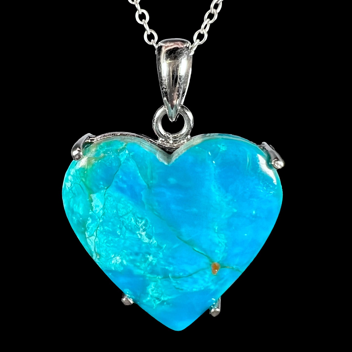 A vibrant Chilean blue opal heart necklace with silver prongs, shown in a macro front view with subtle red flash.