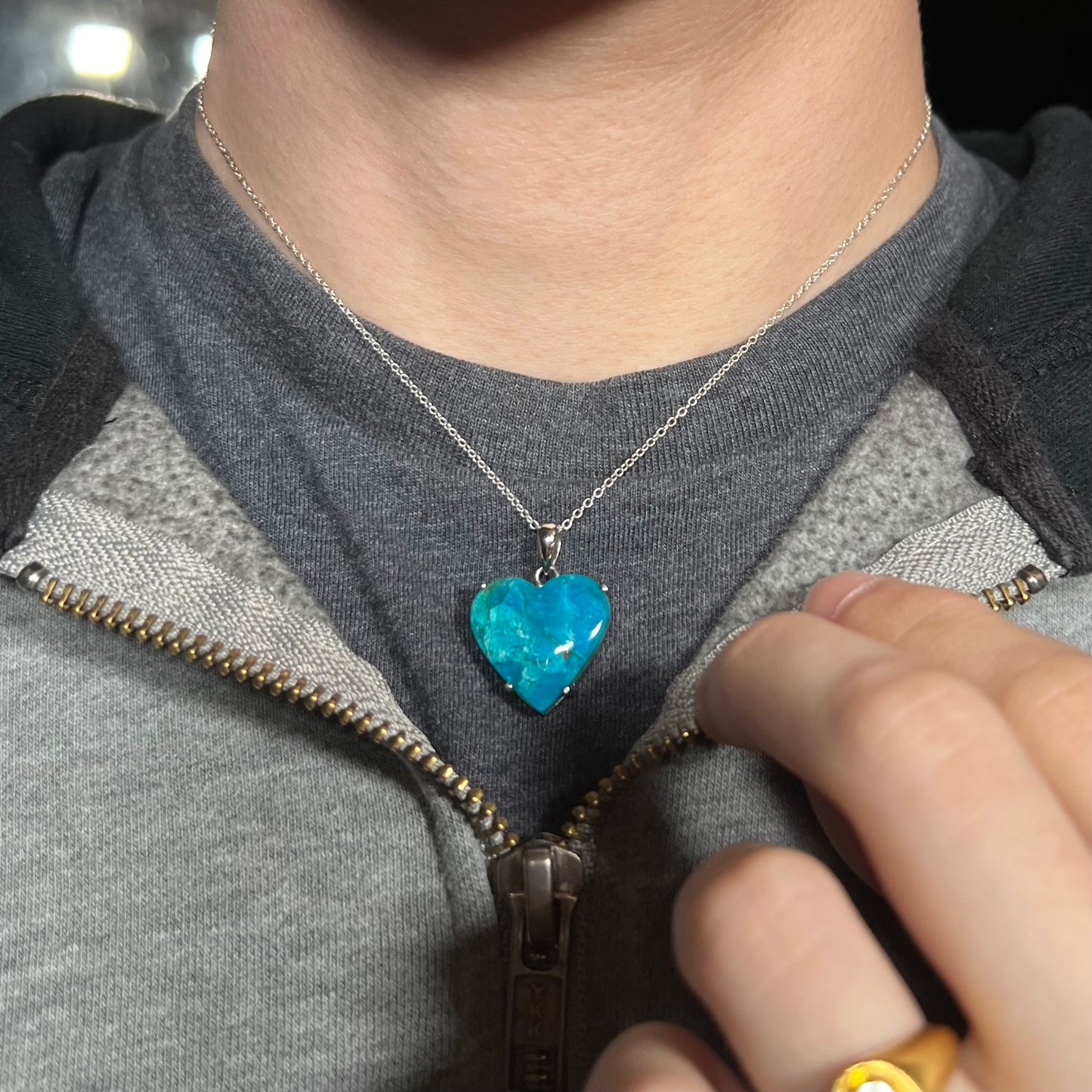 Blue opal heart necklace worn with a zipped sweatshirt and dark shirt, showing casual wear.