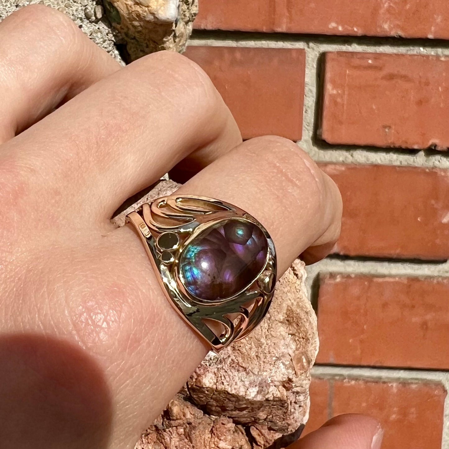 An oval cabochon cut fire agate with purple and blue colors set in a yellow gold men's ring.
