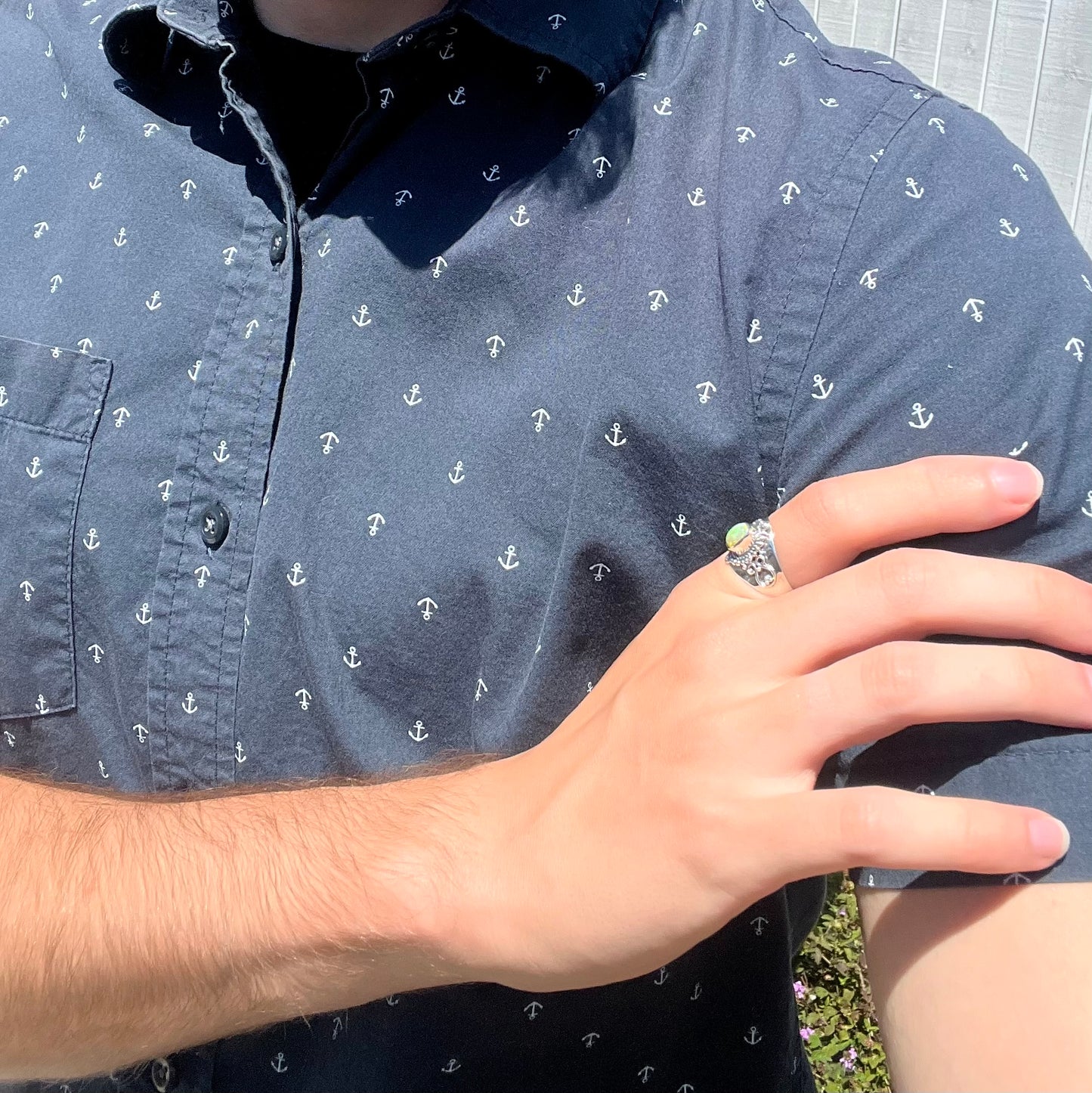 A Boho opal ring worn on the index finger of a hand in sunlight; the hand rests on the model's opposing shoulder.