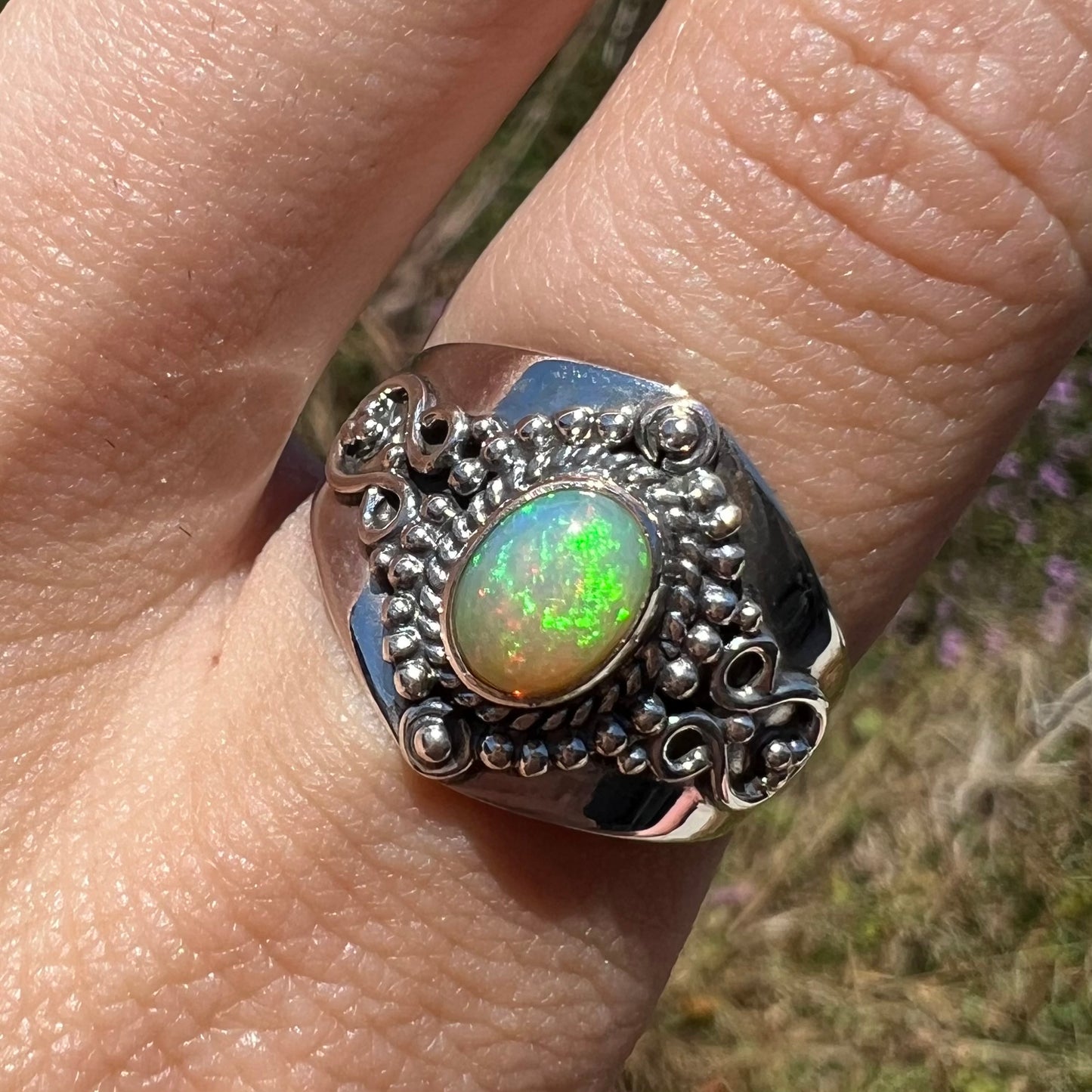 Close-up of the front of a Boho-style opal ring with green fire, worn in the sunlight.