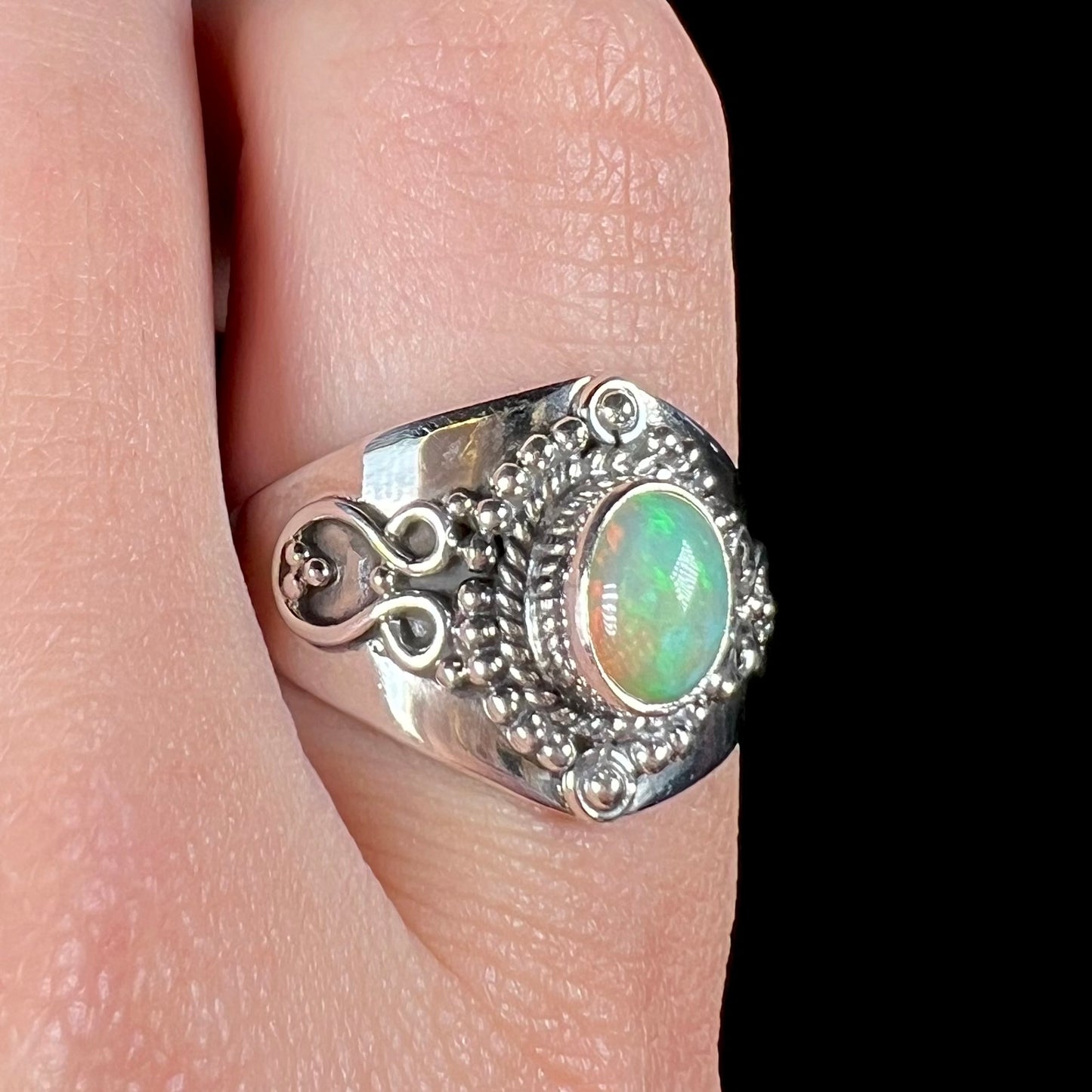 Macro view of a sterling silver Boho-style opal ring, worn on a finger.