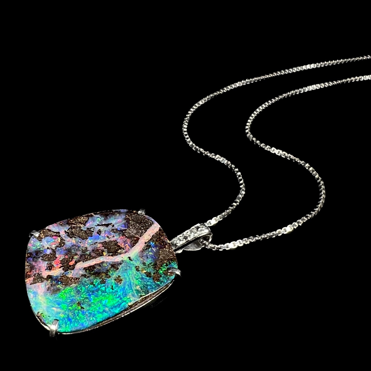Stylized angled shot of a boulder opal diamond pendant against black background, with intense blue and green opal fire facing the camera.