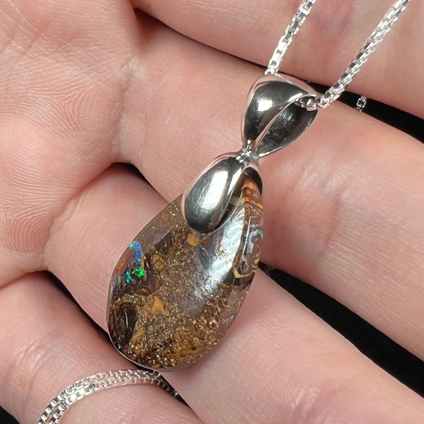 An Australian boulder opal necklace with a sterling silver bail. The opal has a bright green flash of color.