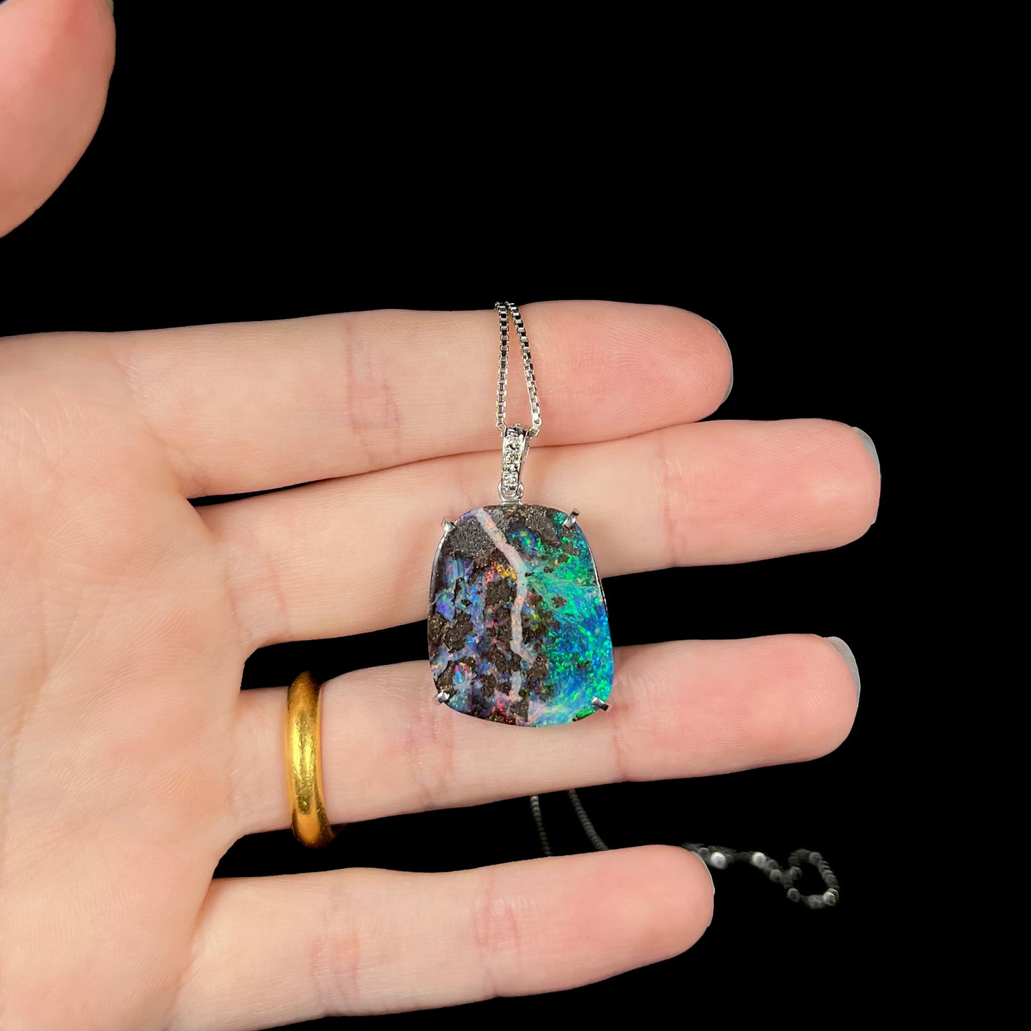 Boulder opal pendant resting on fingers, highlighting its organic ironstone inclusions and natural play-of-color.