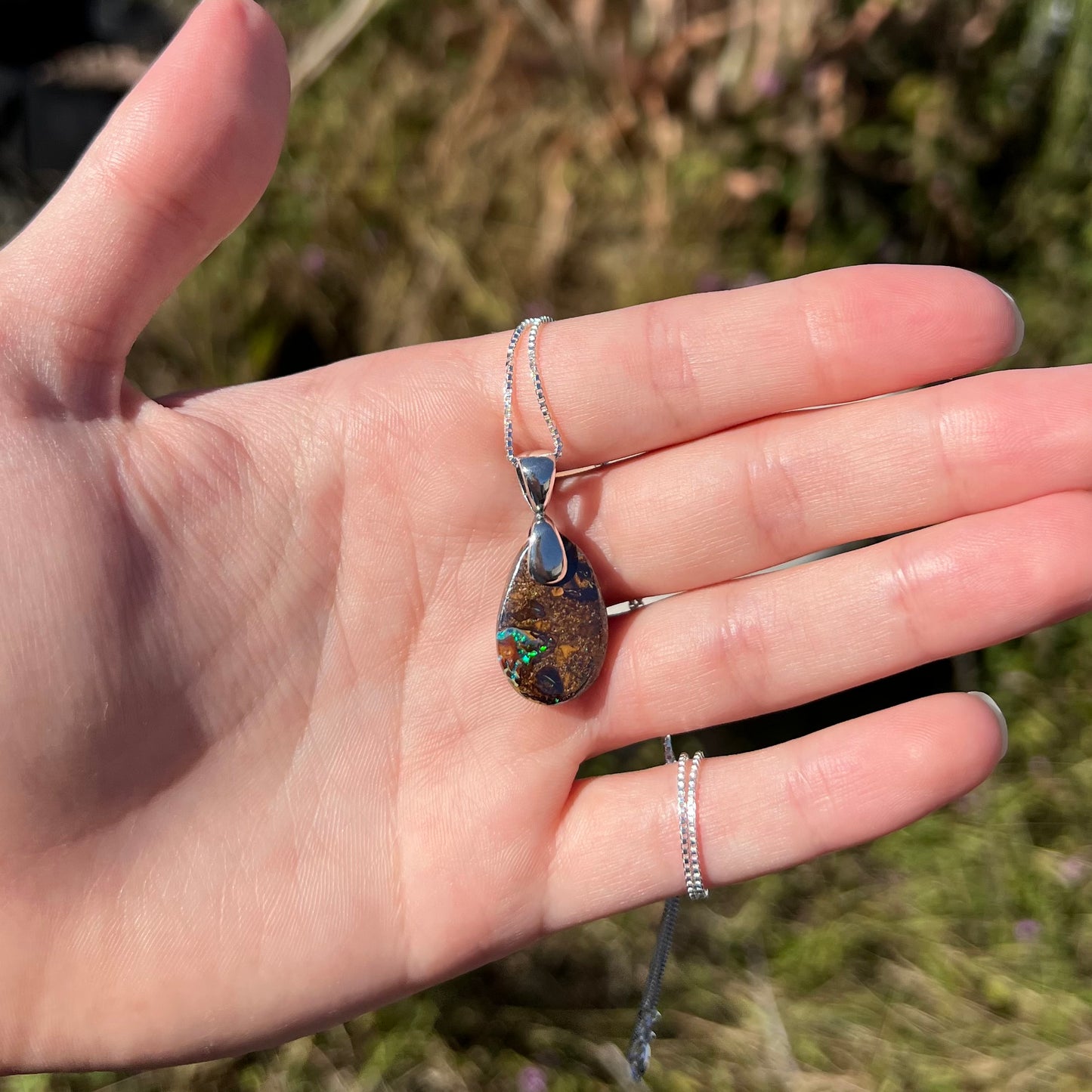 An Australian boulder opal necklace with a sterling silver bail. The opal has a bright green flash of color.
