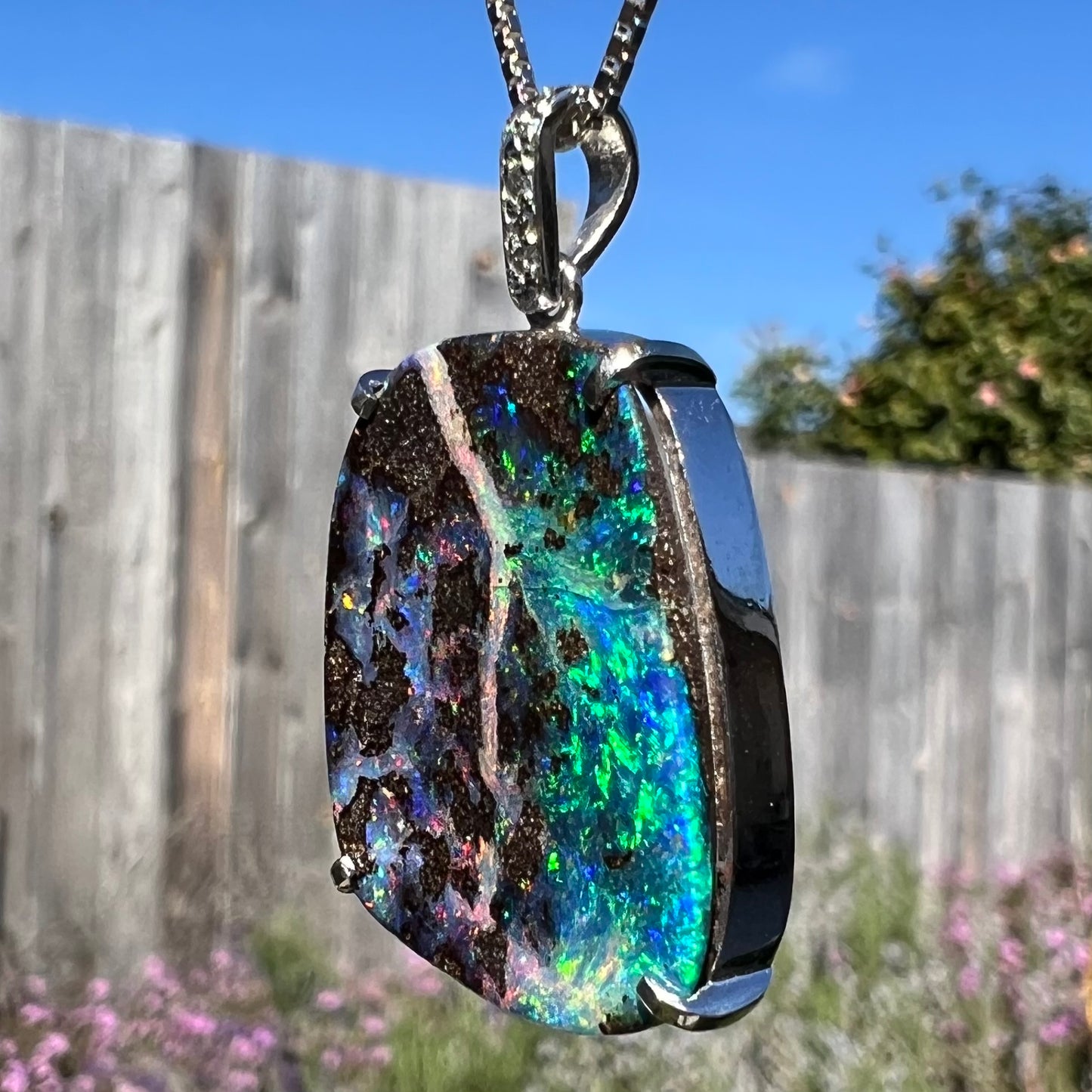 Angled macro shot of a boulder opal pendant in sunlight, revealing its blue and green color play.