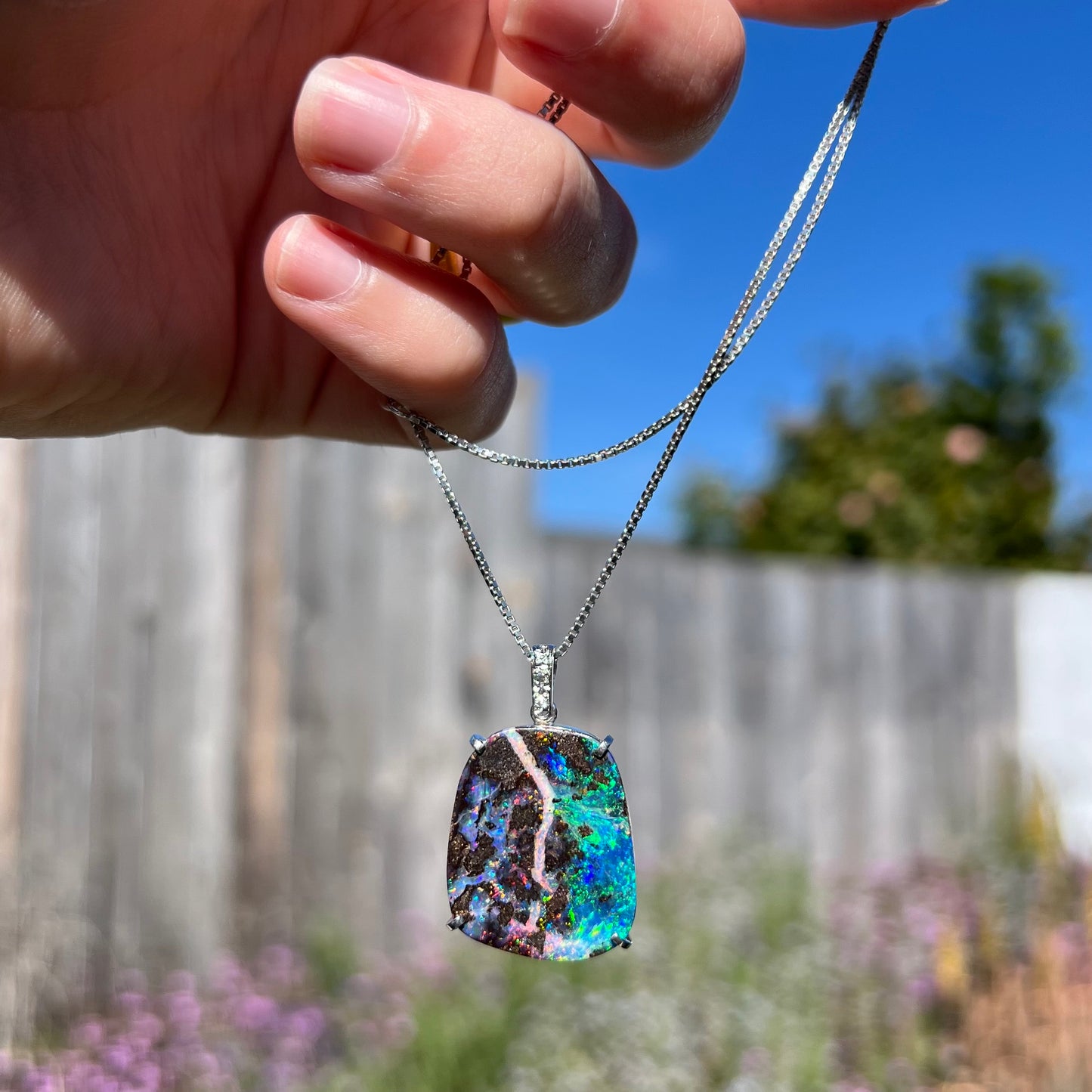 Platinum boulder opal pendant dangling in natural sunlight, with strong contrast between its two distinct color zones.