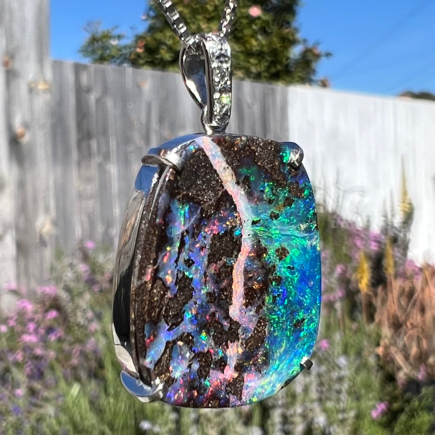 Macro shot of a boulder opal pendant in sunlight, highlighting the opal’s purple and pink hues.