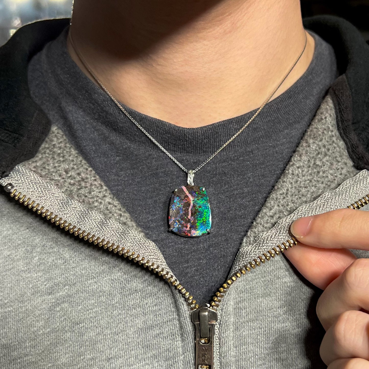 Boulder opal necklace worn on a black t-shirt with a partially zipped sweatshirt, showing its striking fire.