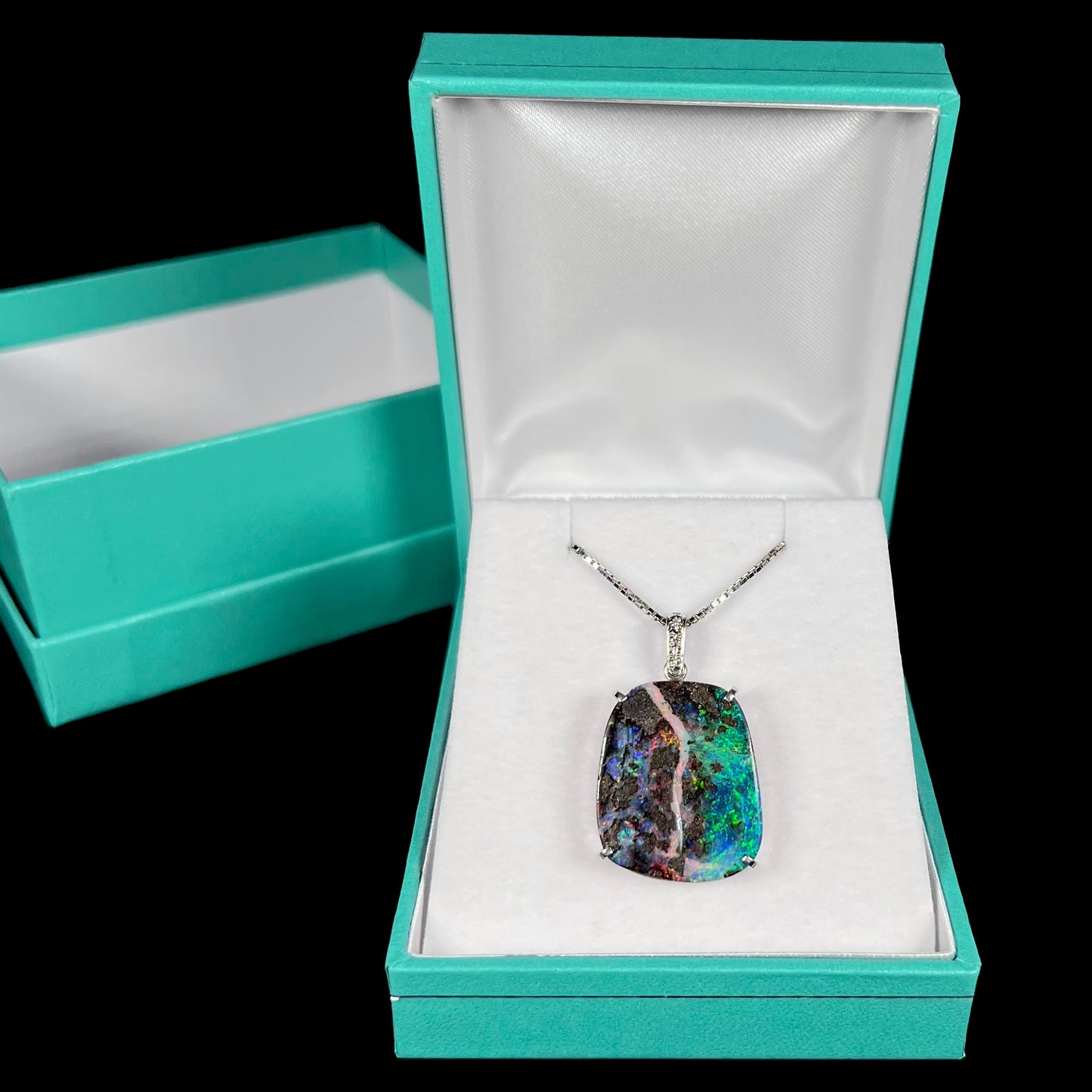 Platinum boulder opal pendant in a blue jewelry box, displayed against a black background.