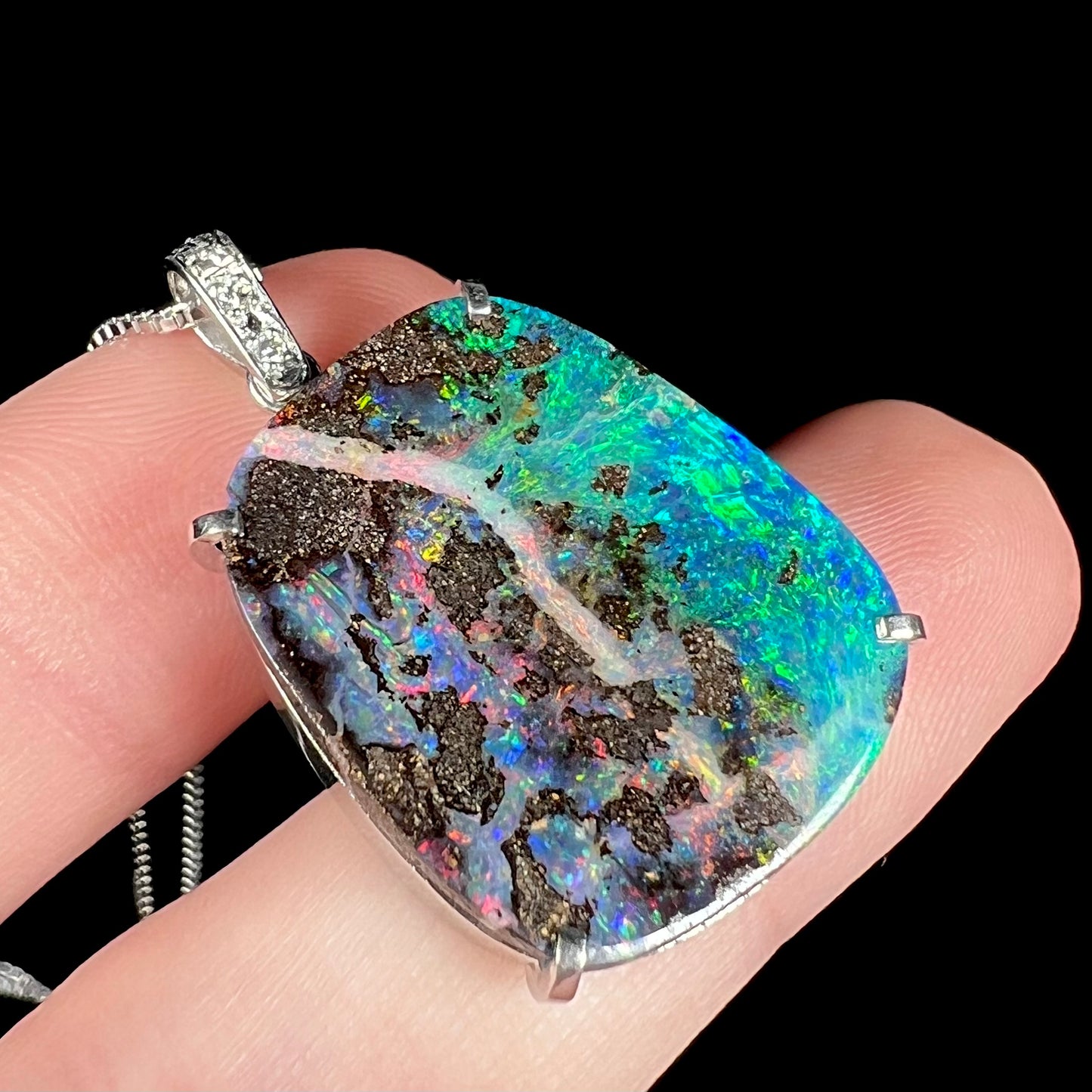 Angled macro close-up of a platinum boulder opal pendant, with purplish-red hues facing the camera.