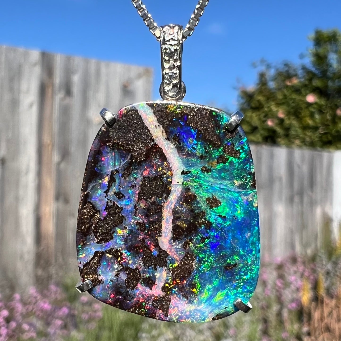 Macro close-up of boulder opal pendant in sunlight, showing intense green flashes.