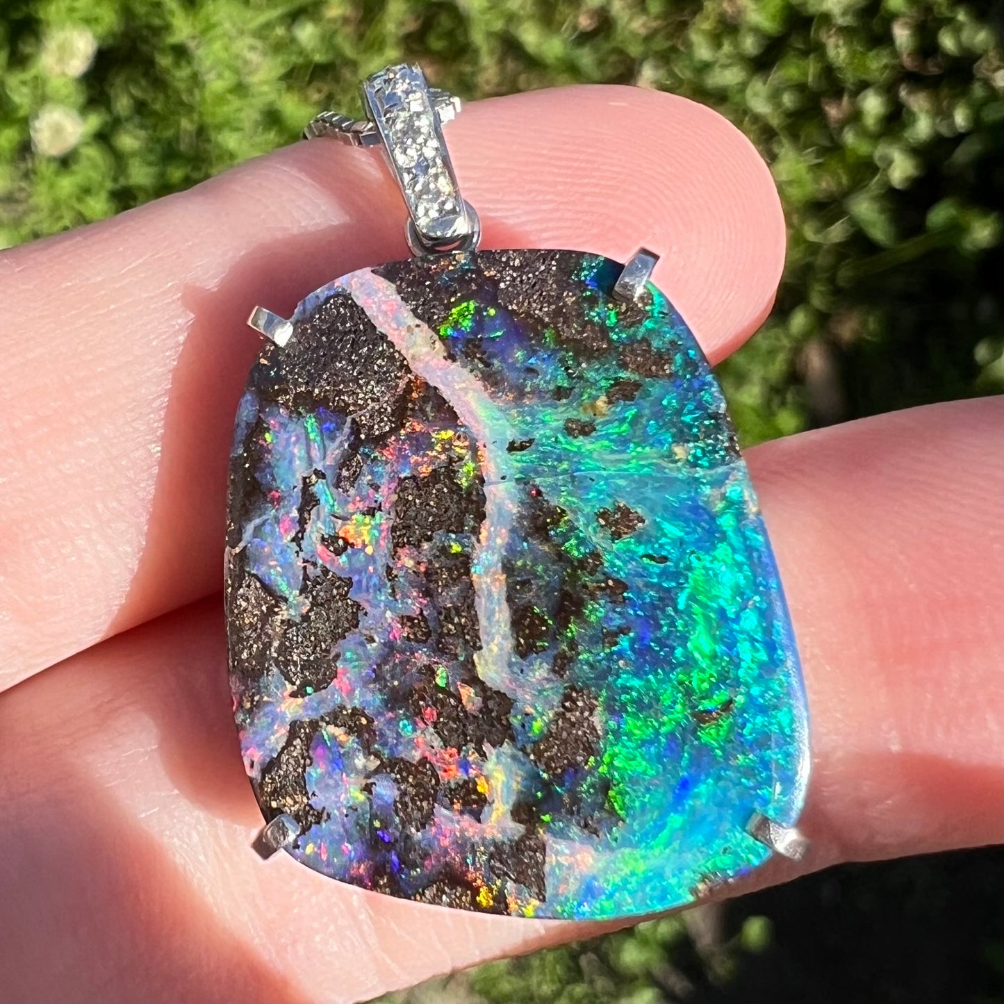 Straight-on macro close-up of a platinum boulder opal pendant in sunlight, with exceptionally vibrant multicolor fire.