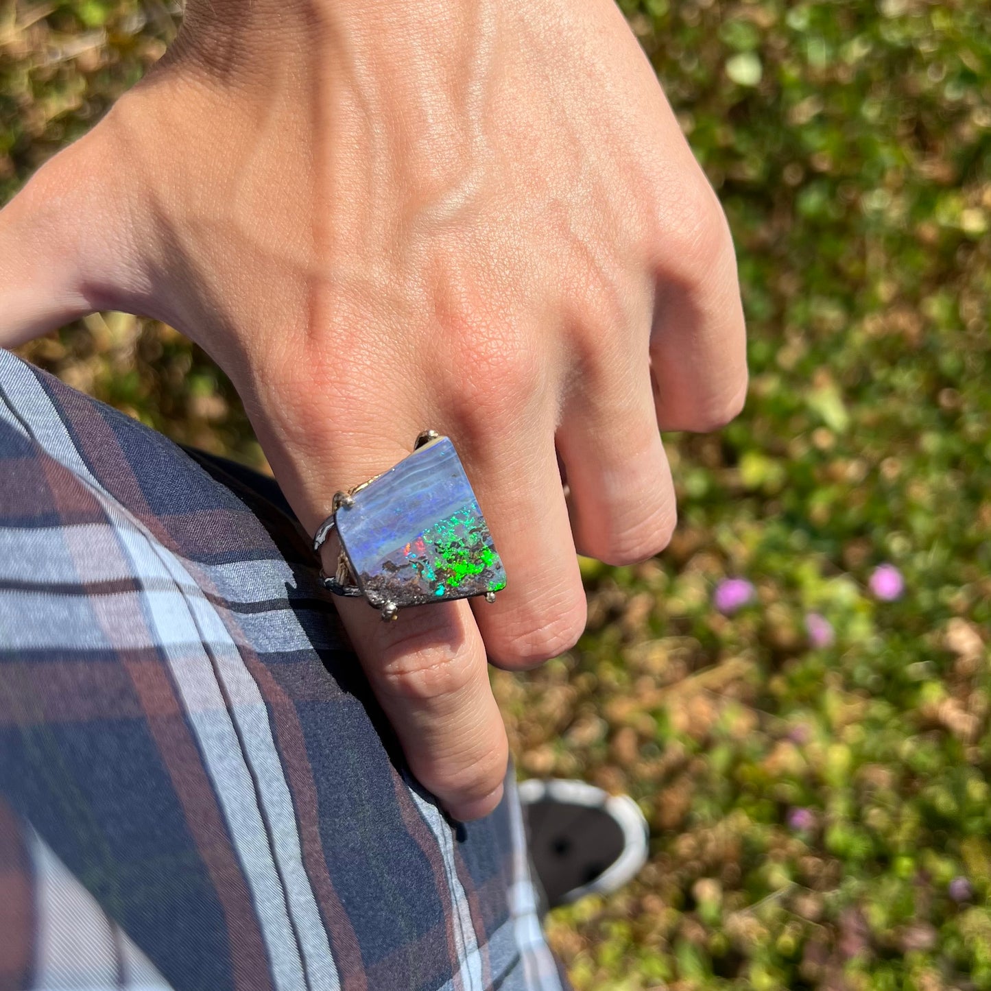 A person resting their hand on their hip in sunlight while wearing a boulder opal ring with bright green flashes.