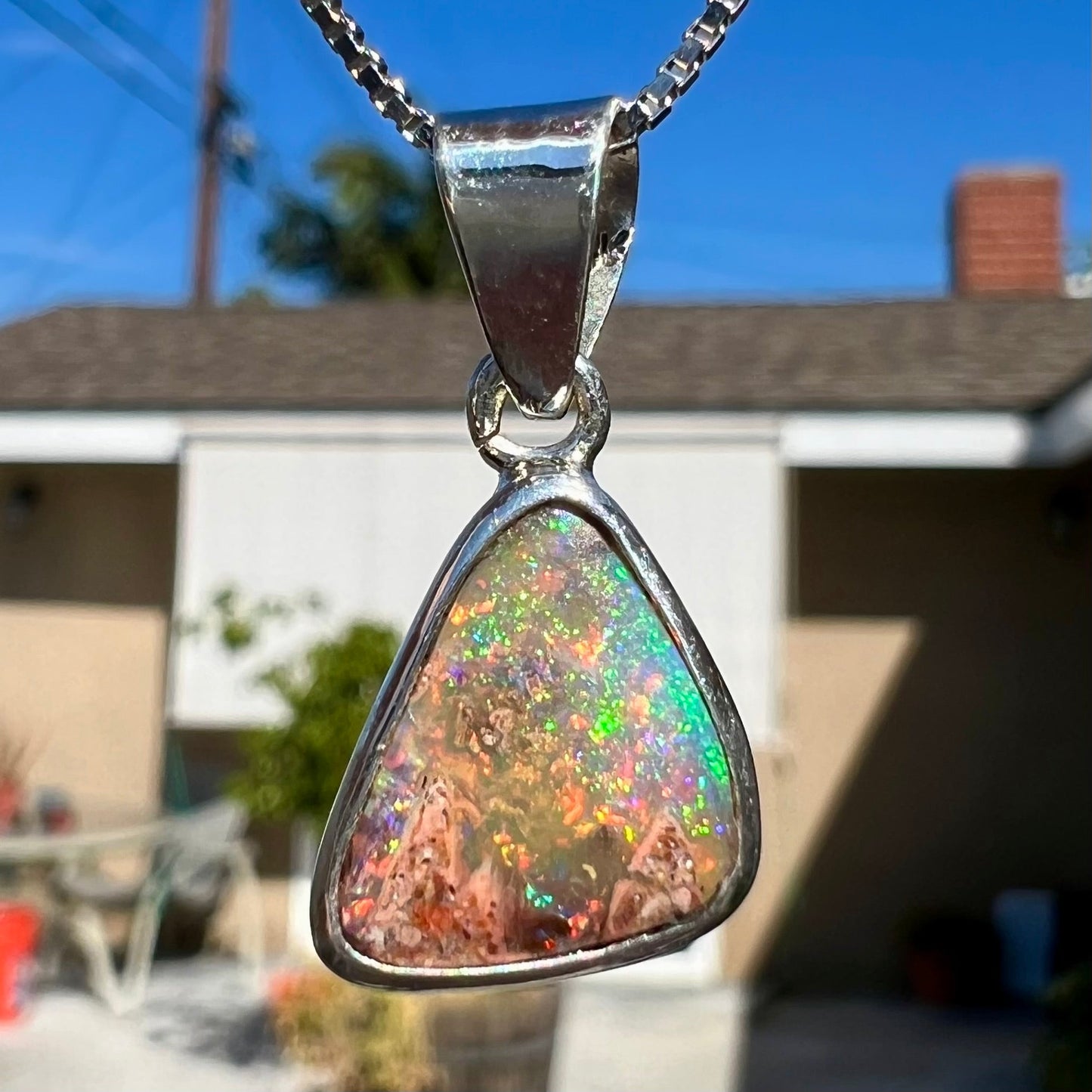 A sterling silver boulder opal necklace on a box chain. The opal twinkles bright red, green, and blue colors.