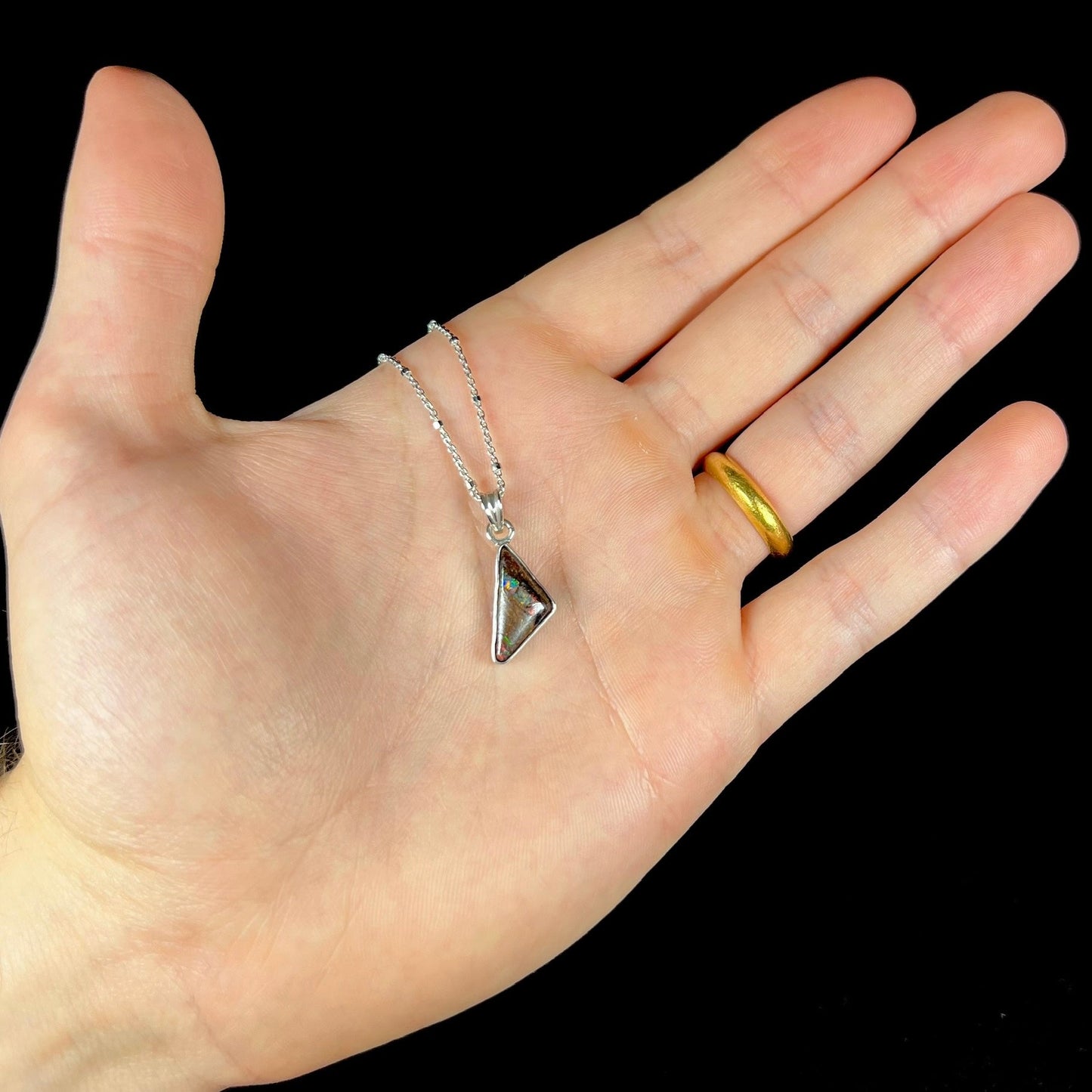 A triangle shaped opal necklace in sterling silver.  The opal shines with every color of the rainbow.