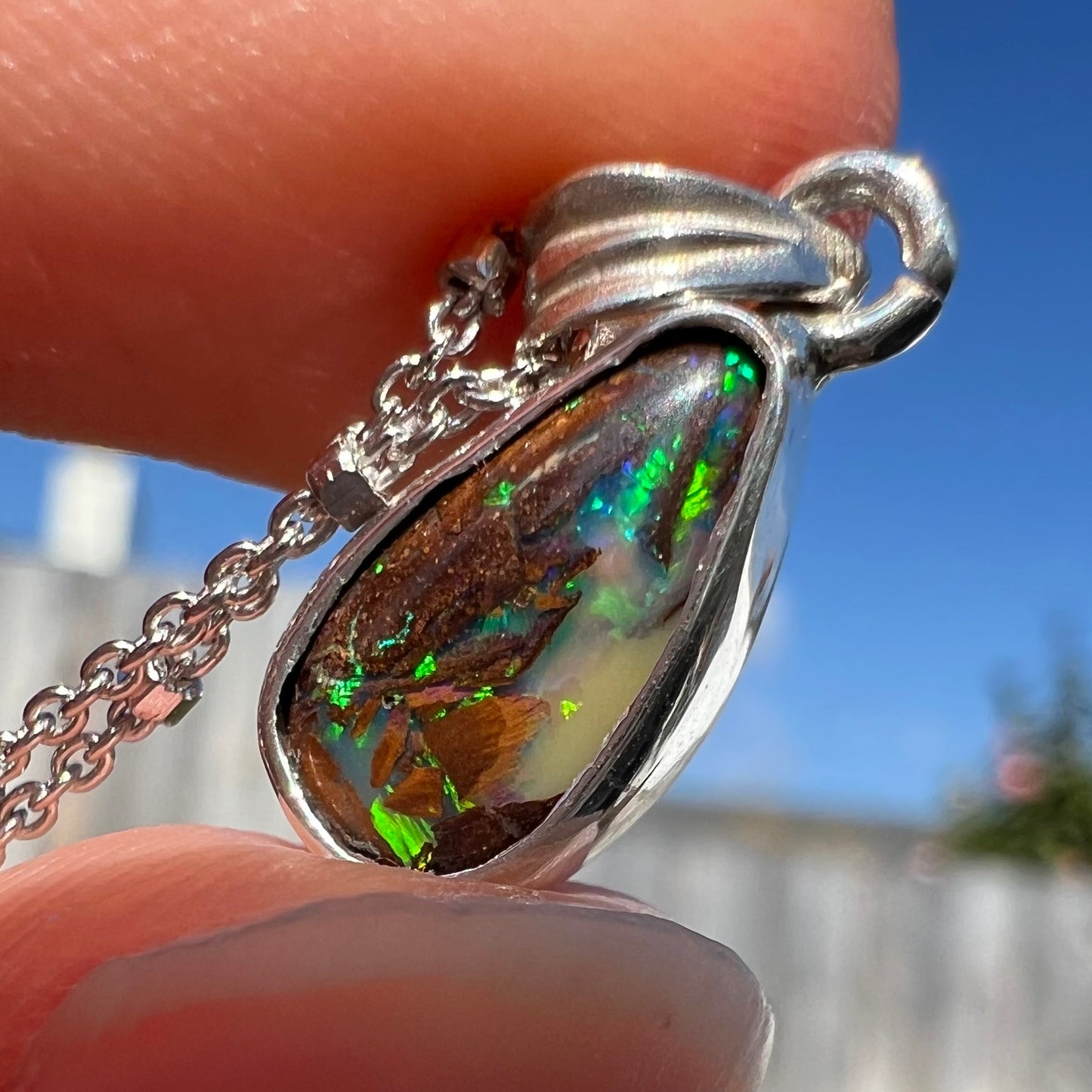 A pear shaped boulder opal necklace in sterling silver. The opal has bright green and blue flashes.