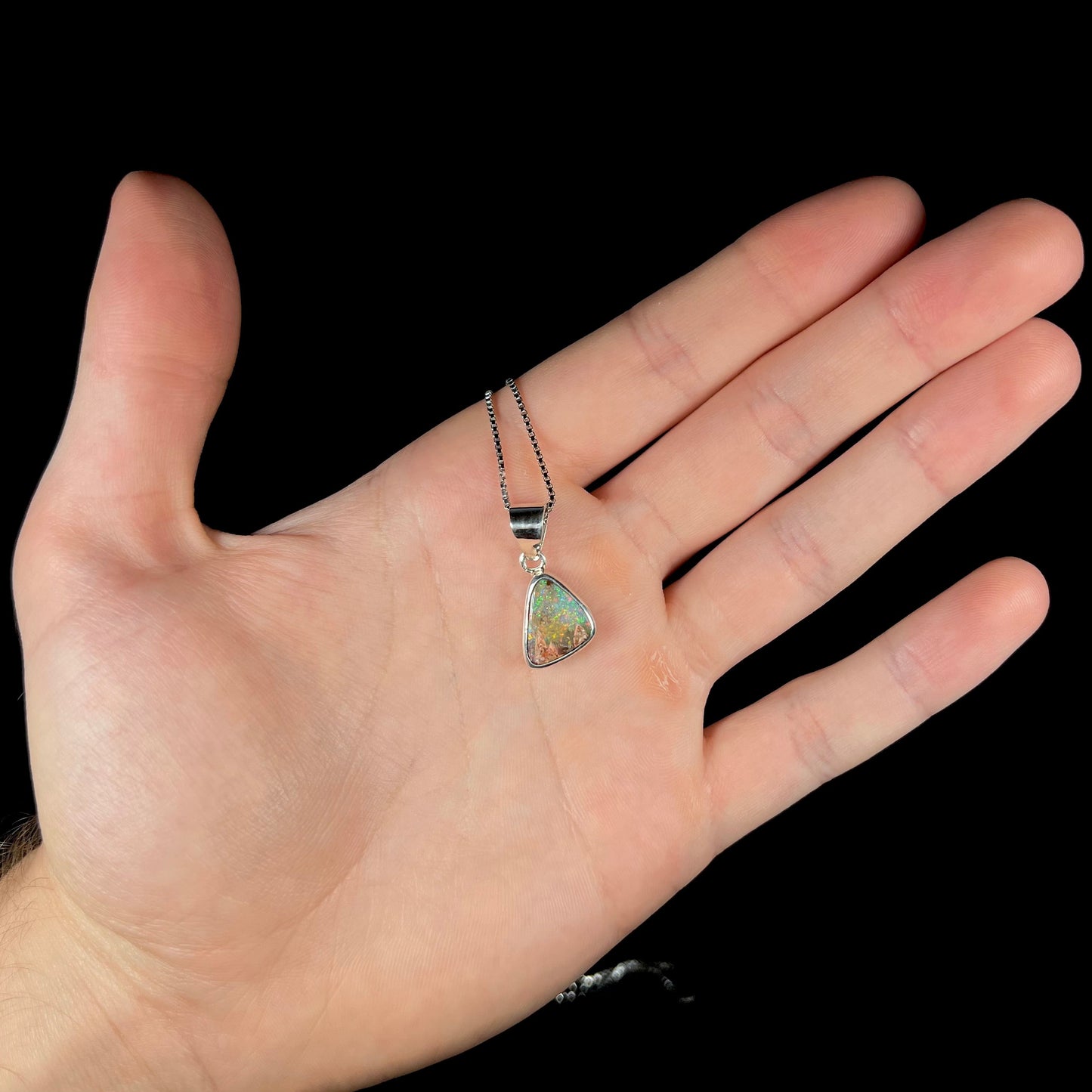 A sterling silver boulder opal necklace on a box chain. The opal twinkles bright red, green, and blue colors.