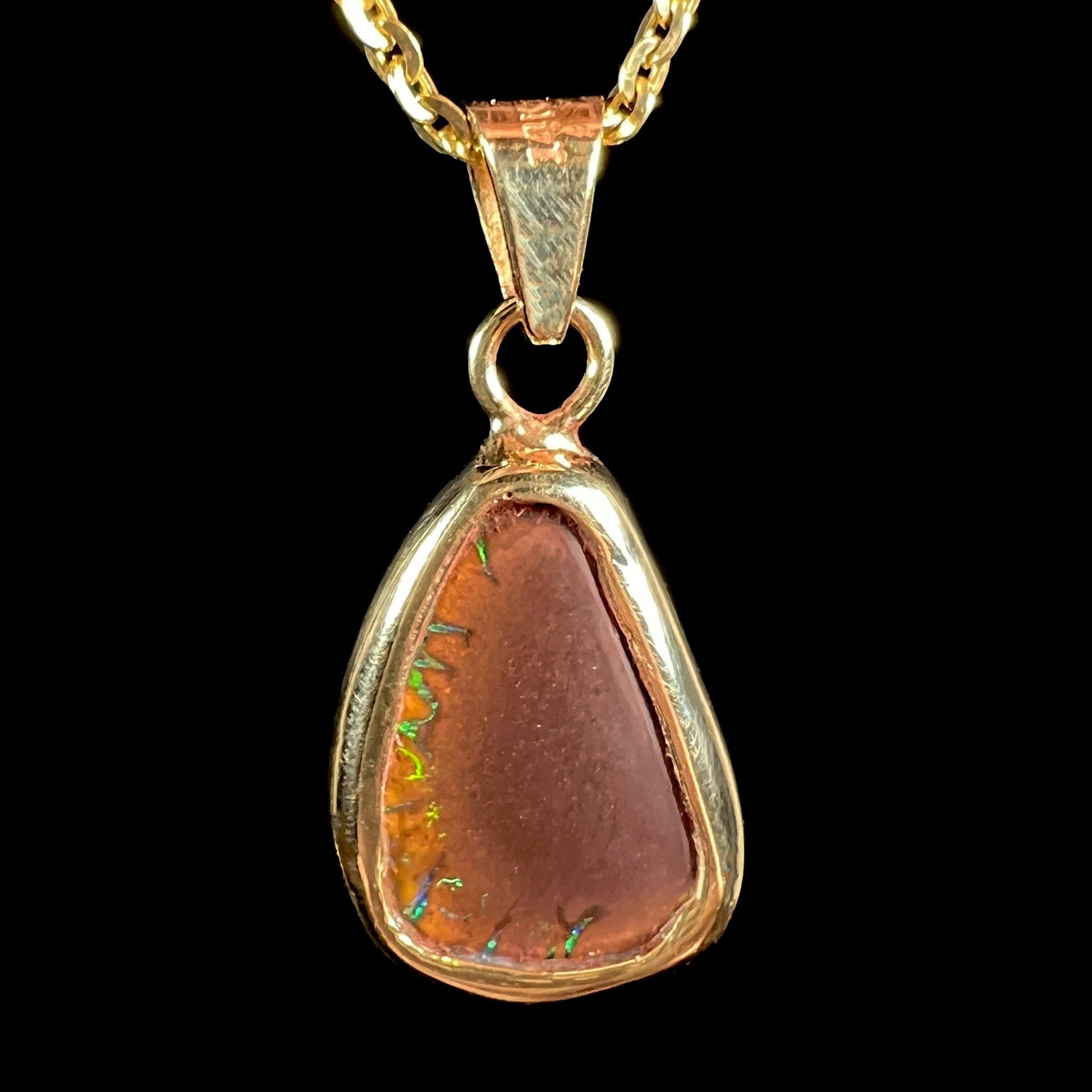 A ladies' natural boulder opal necklace set in 14k yellow gold.  The opal is bezel set and shows green and blue colors.
