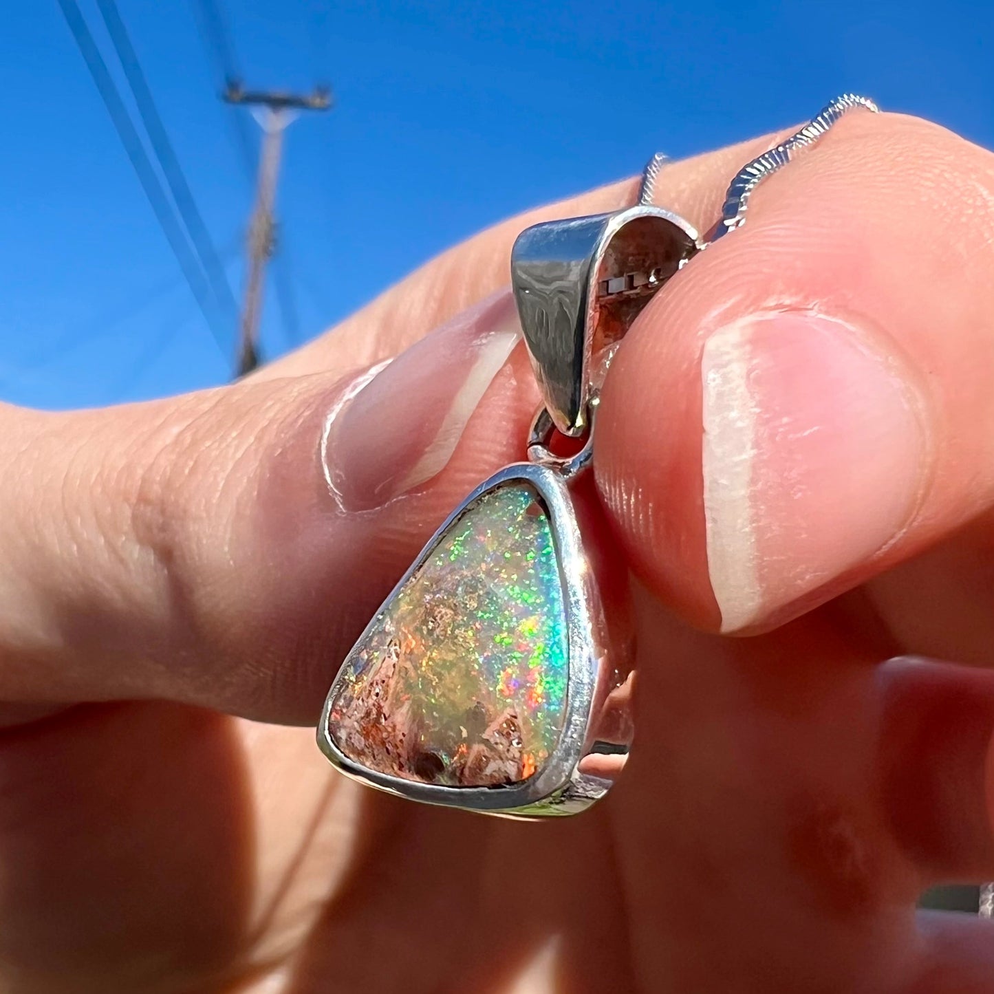 A sterling silver boulder opal necklace on a box chain. The opal twinkles bright red, green, and blue colors.