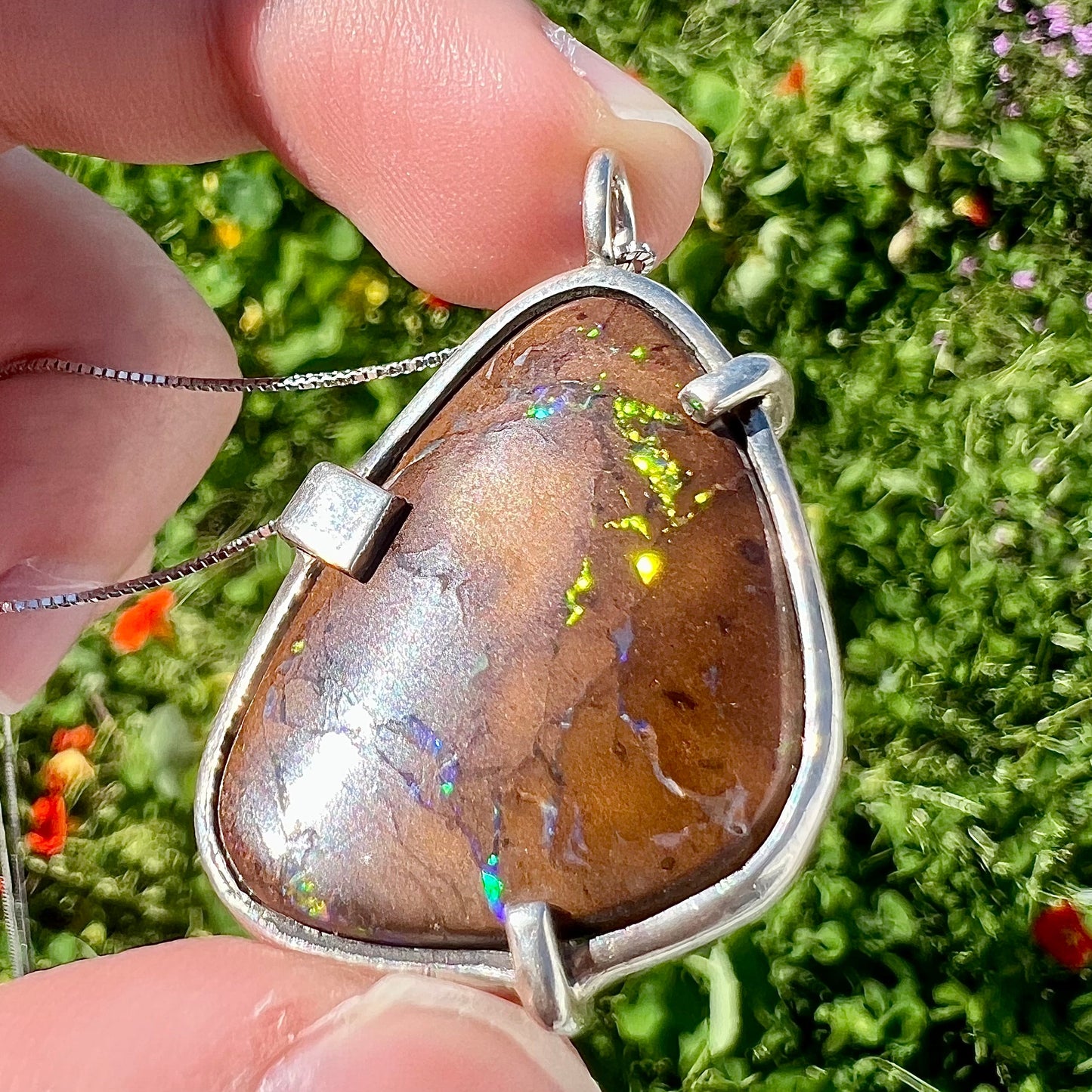 A handmade sterling silver pendant bezel and prong set with a natural boulder opal stone. The opal shines veins of color.