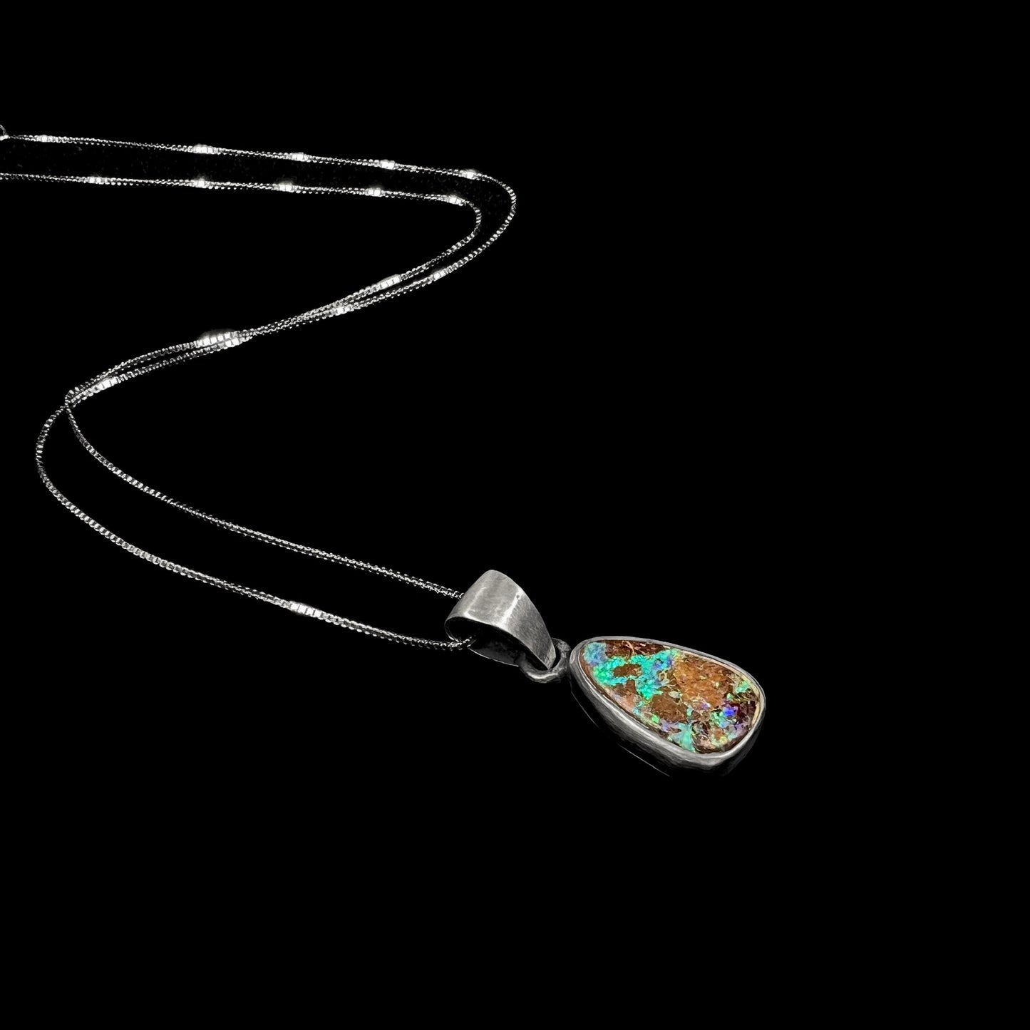 A handmade, satin finish sterling silver pendant set with a drop shaped boulder opal stone.