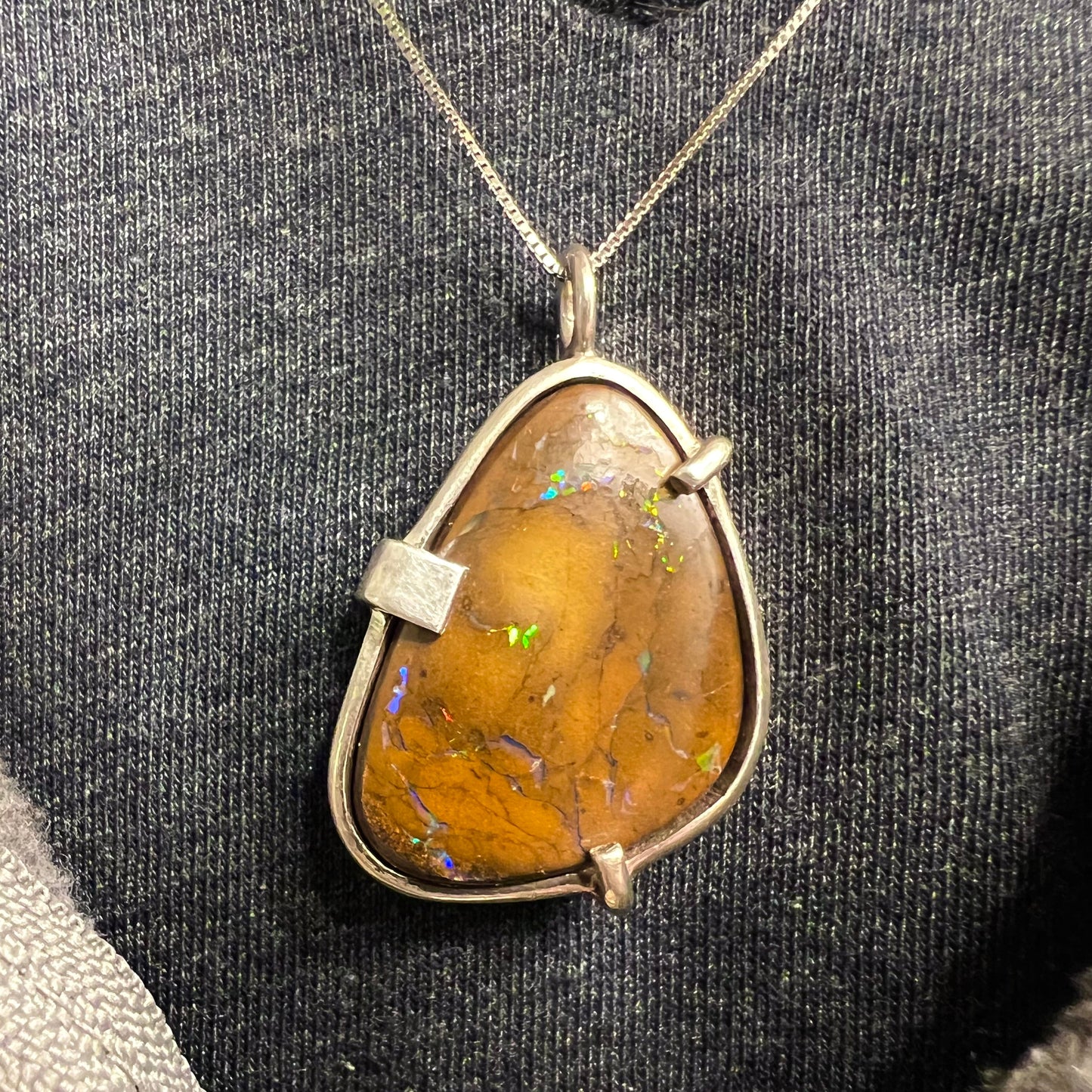 A handmade sterling silver pendant bezel and prong set with a natural boulder opal stone. The opal shines veins of color.