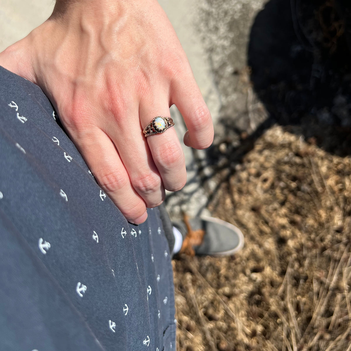 Close-up of person's hand resting on their hip in sunlight while wearing a brass Australian opal ring
