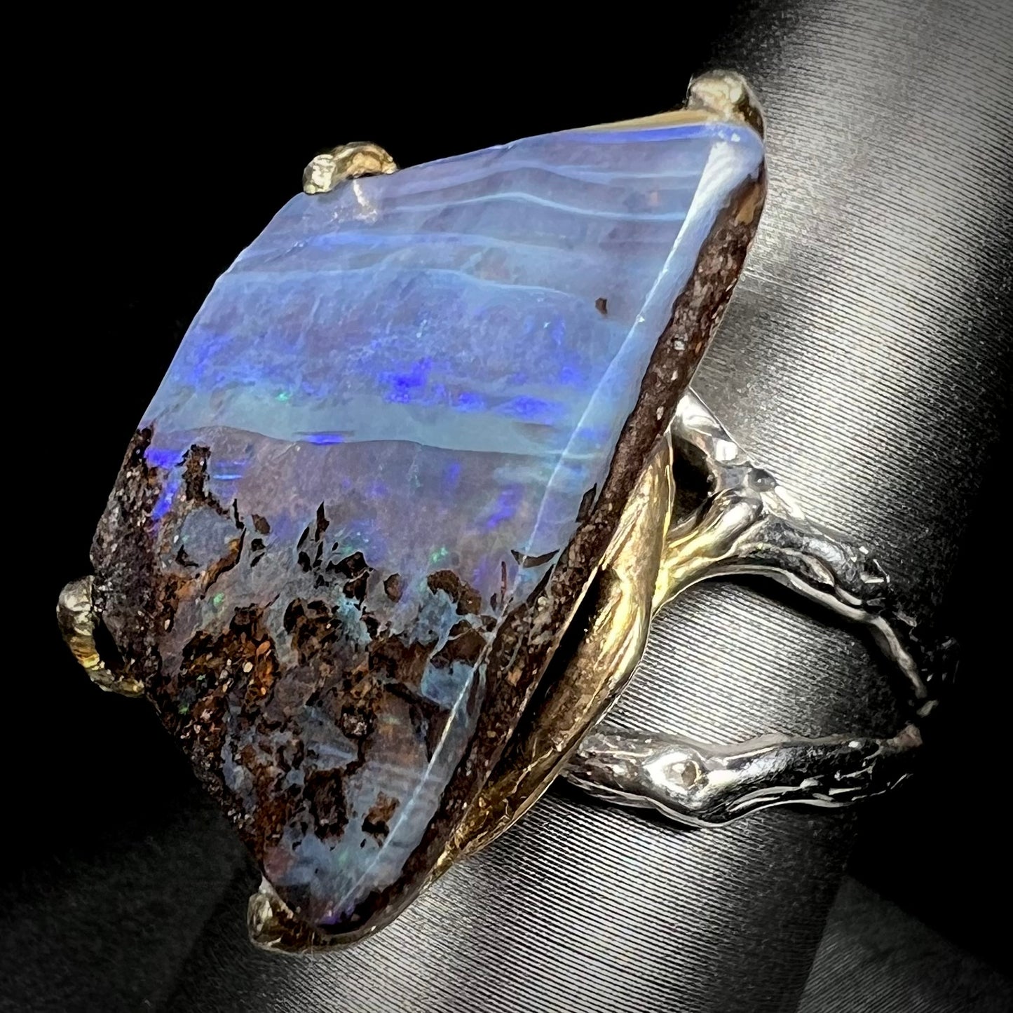 Angled view of a large, brutalist style boulder opal ring in two-tone sterling silver.
