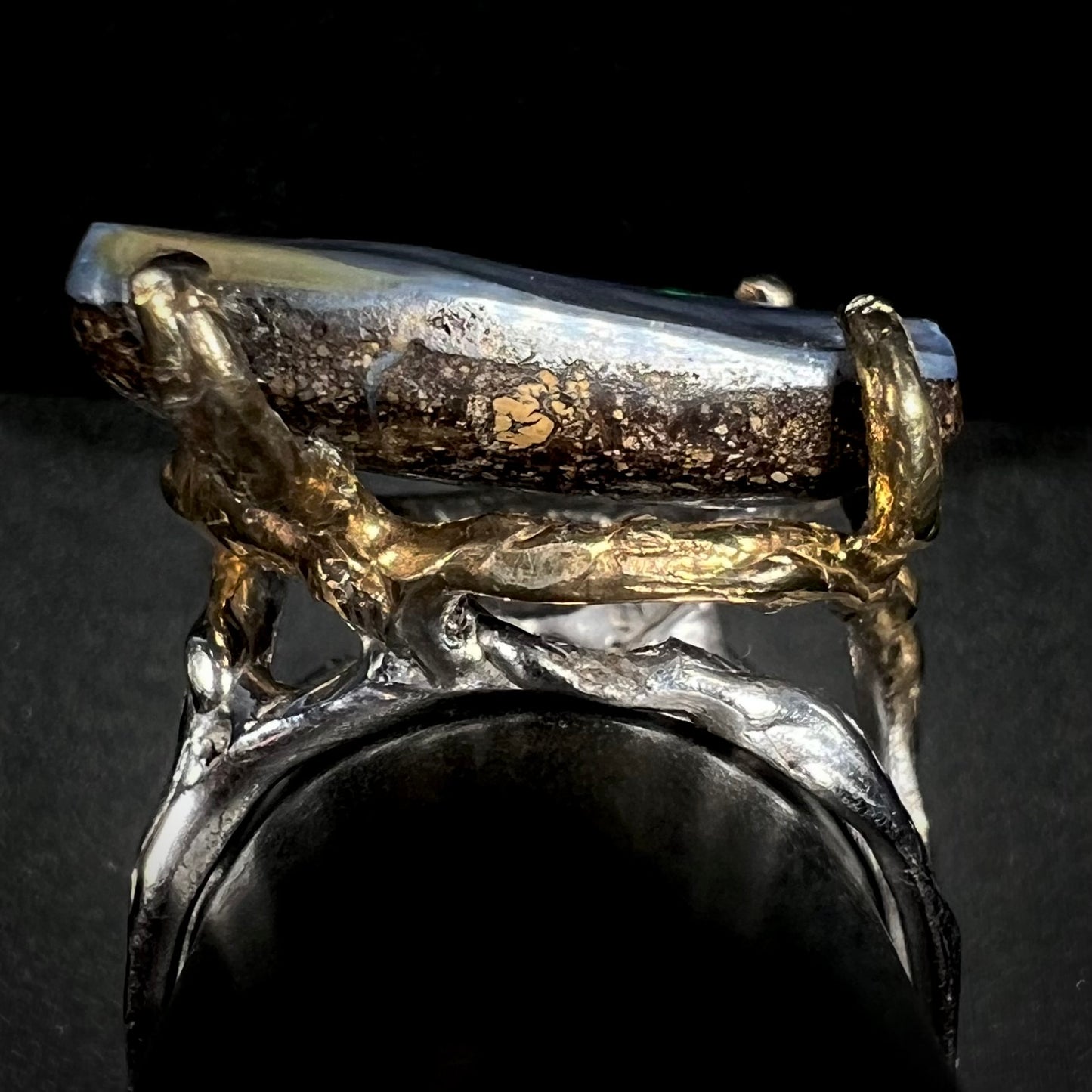 Side profile gallery view of a brutalist-style boulder opal ring with gold prongs and a silver shank.