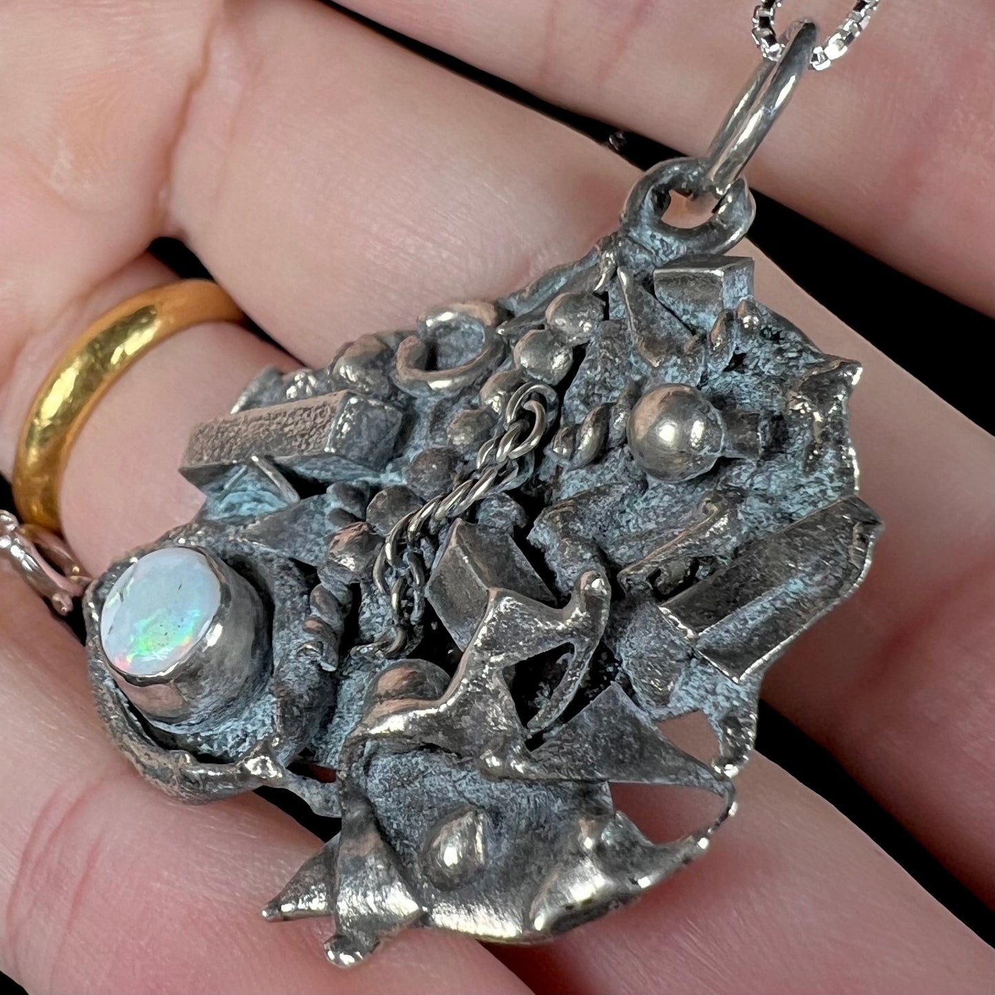 A brutalist scrap silver opal necklace shown close-up in a hand at an angle.