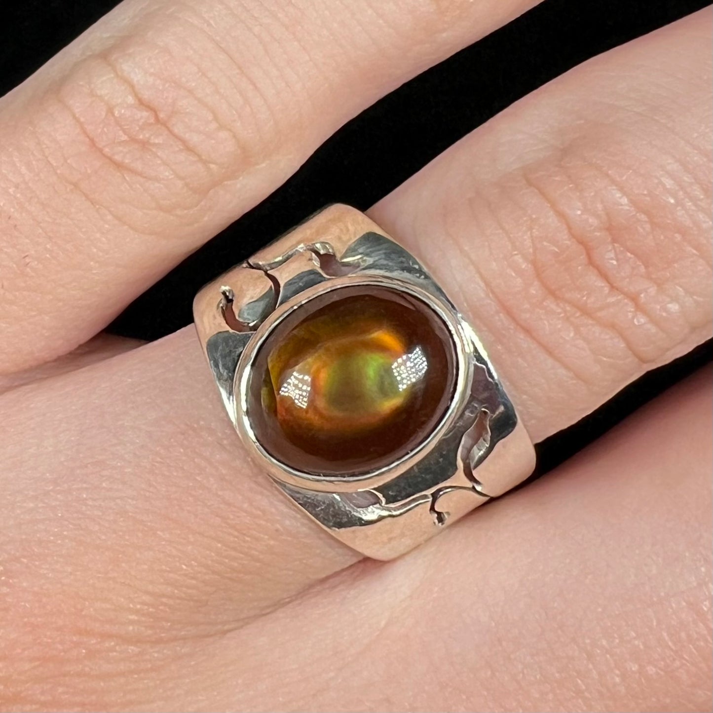 A silver fire agate ring that shows a red and green bull's eye pattern in the stone, shown from the front.