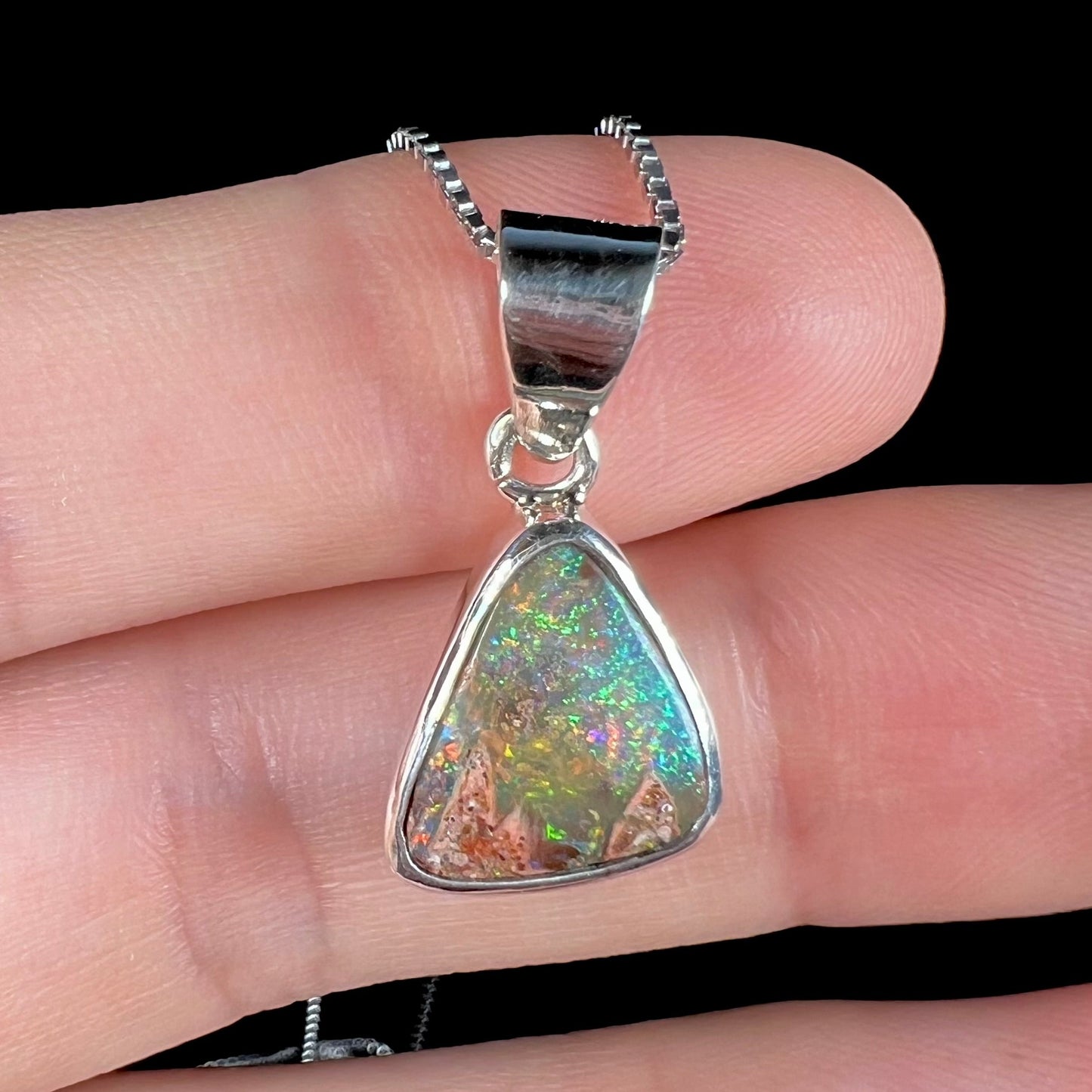 A sterling silver boulder opal necklace on a box chain. The opal twinkles bright red, green, and blue colors.