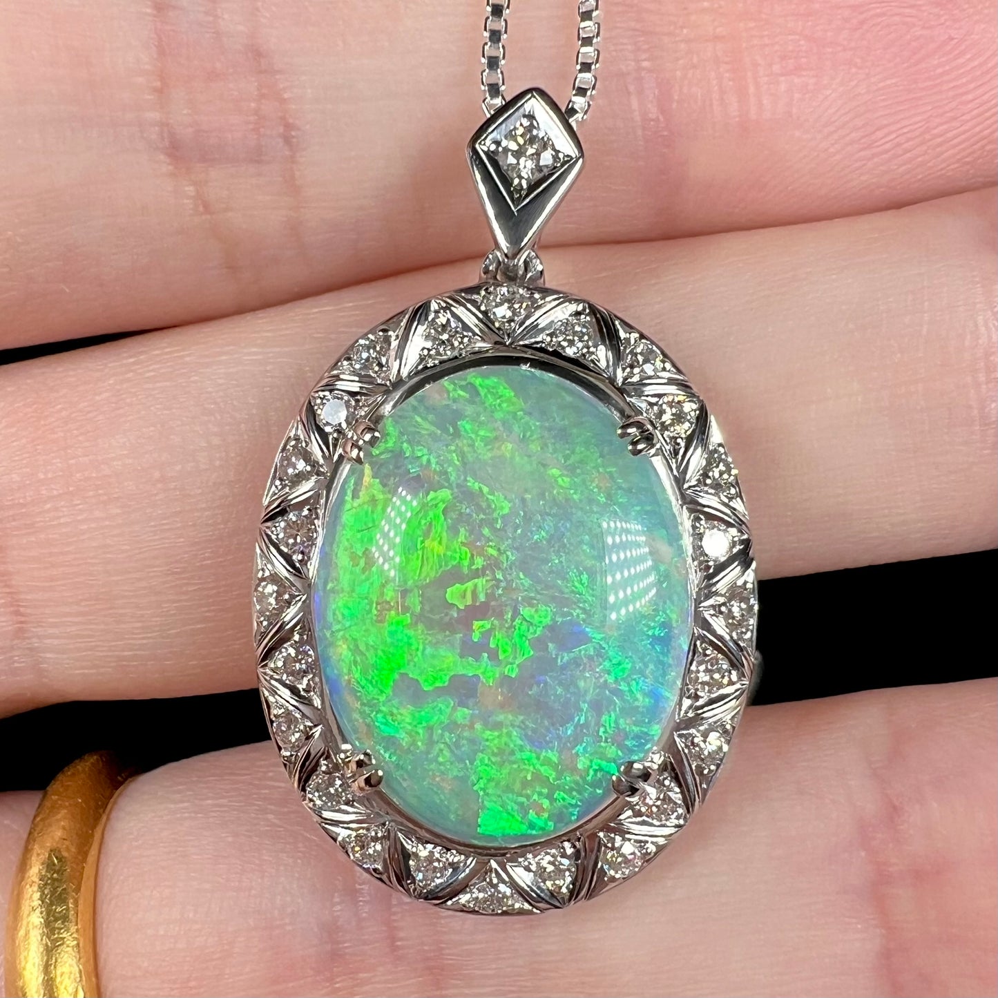 Macro close-up of platinum opal pendant against fingers, showing bright green color play.