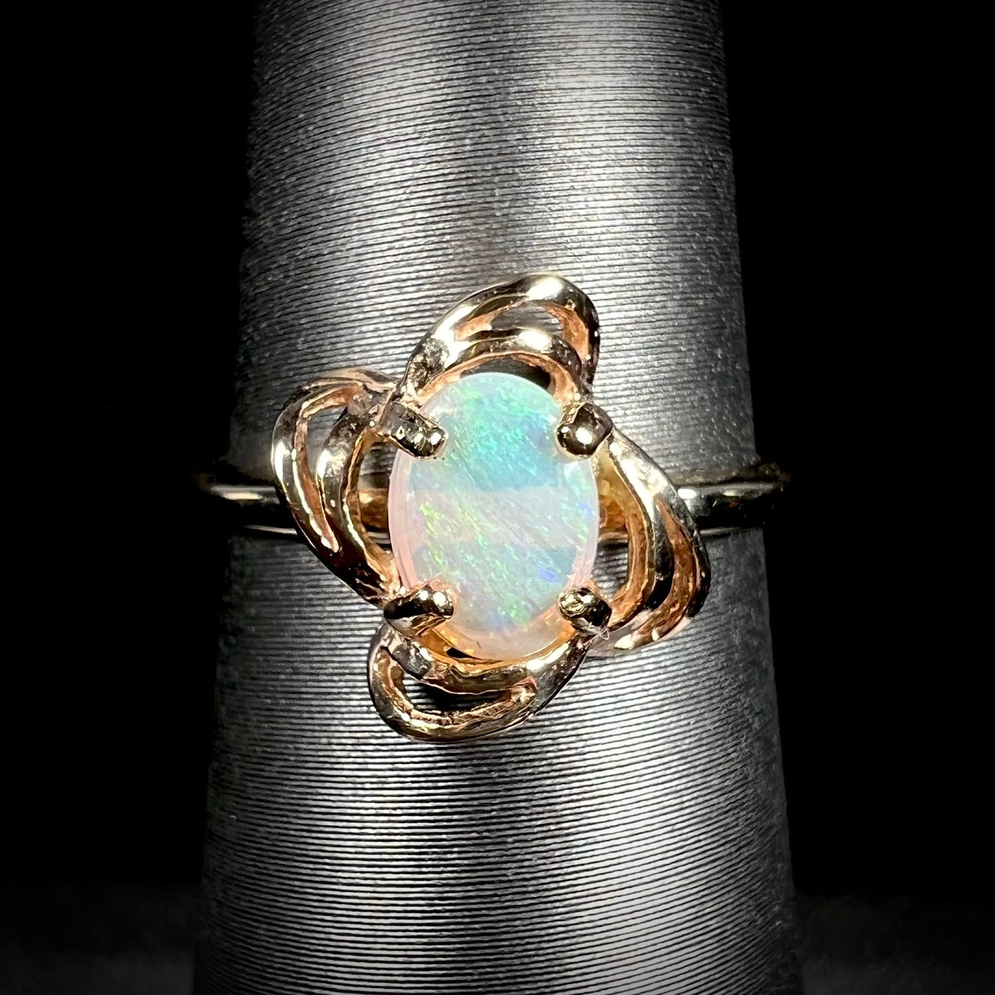 A yellow gold ring mounted with an oval cut opal. The opal has a white base tone with green and blue color play.