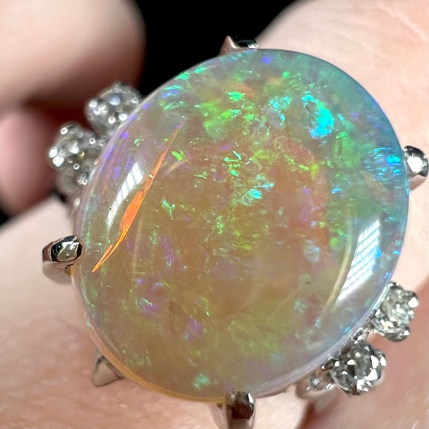 An Australian crystal opal and diamond engagement ring set in a platinum filigree mounting. The opal plays green/blue colors and has a crack.
